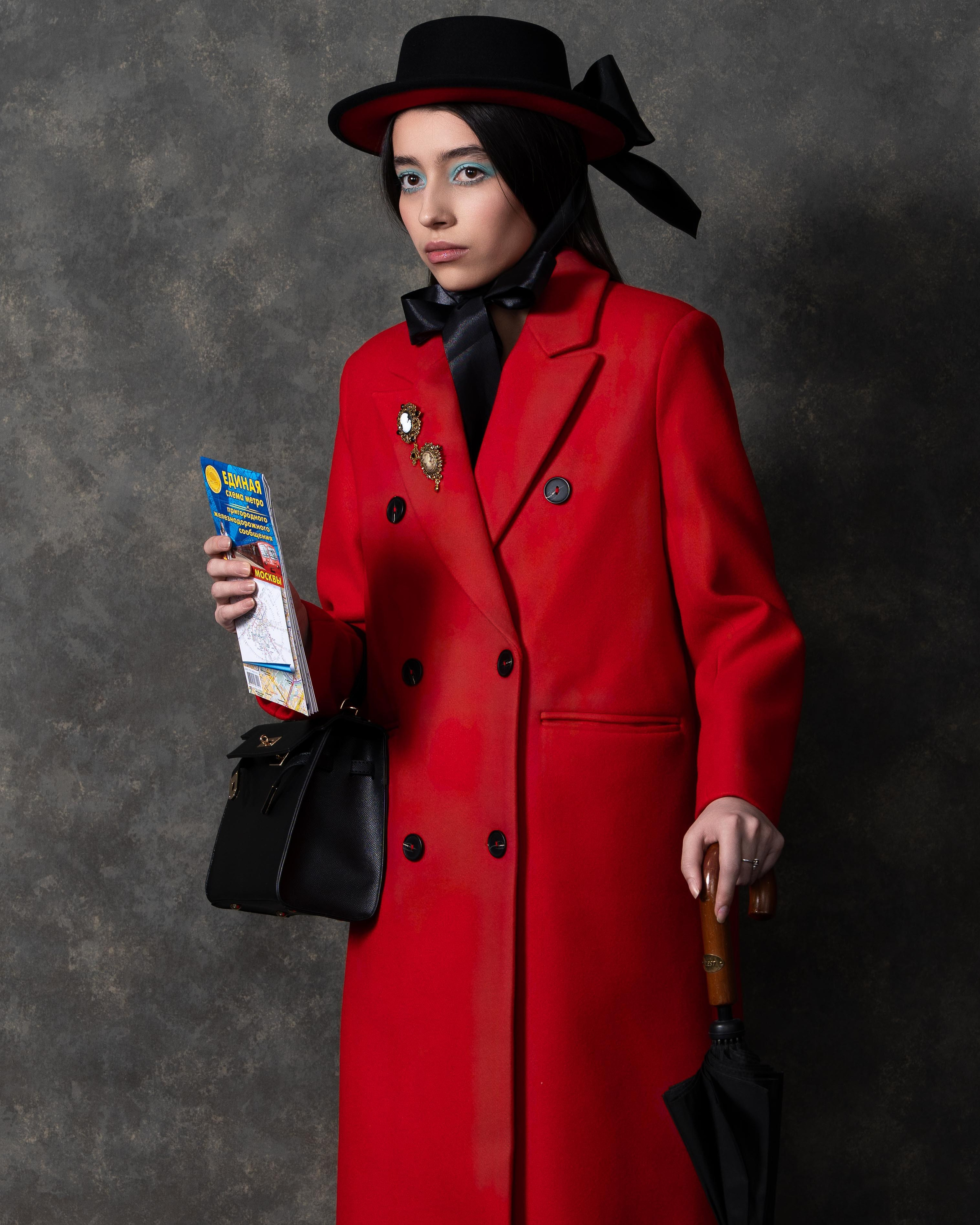 На фотографии изображена женщина в красном пальто и черной шляпе с бантом. Она держит в руках зонт и журнал "Европа Плюс".