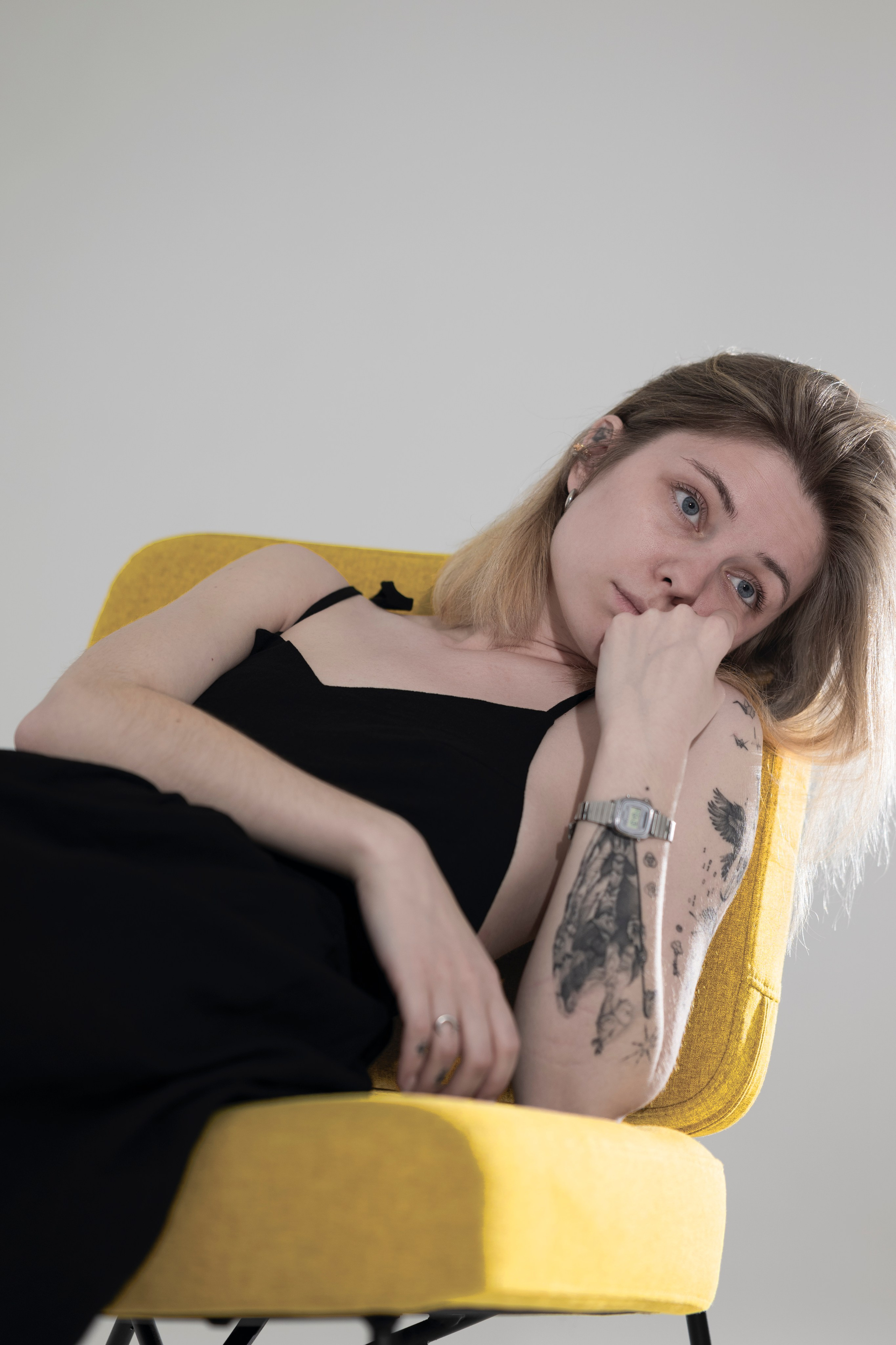 Светловолосая девушка задумчиво сидит на желтом кресле