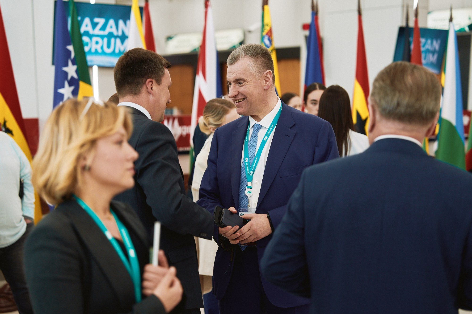 Бизнесмены и дипломаты общаются на KazanForum на фоне национальных флагов.