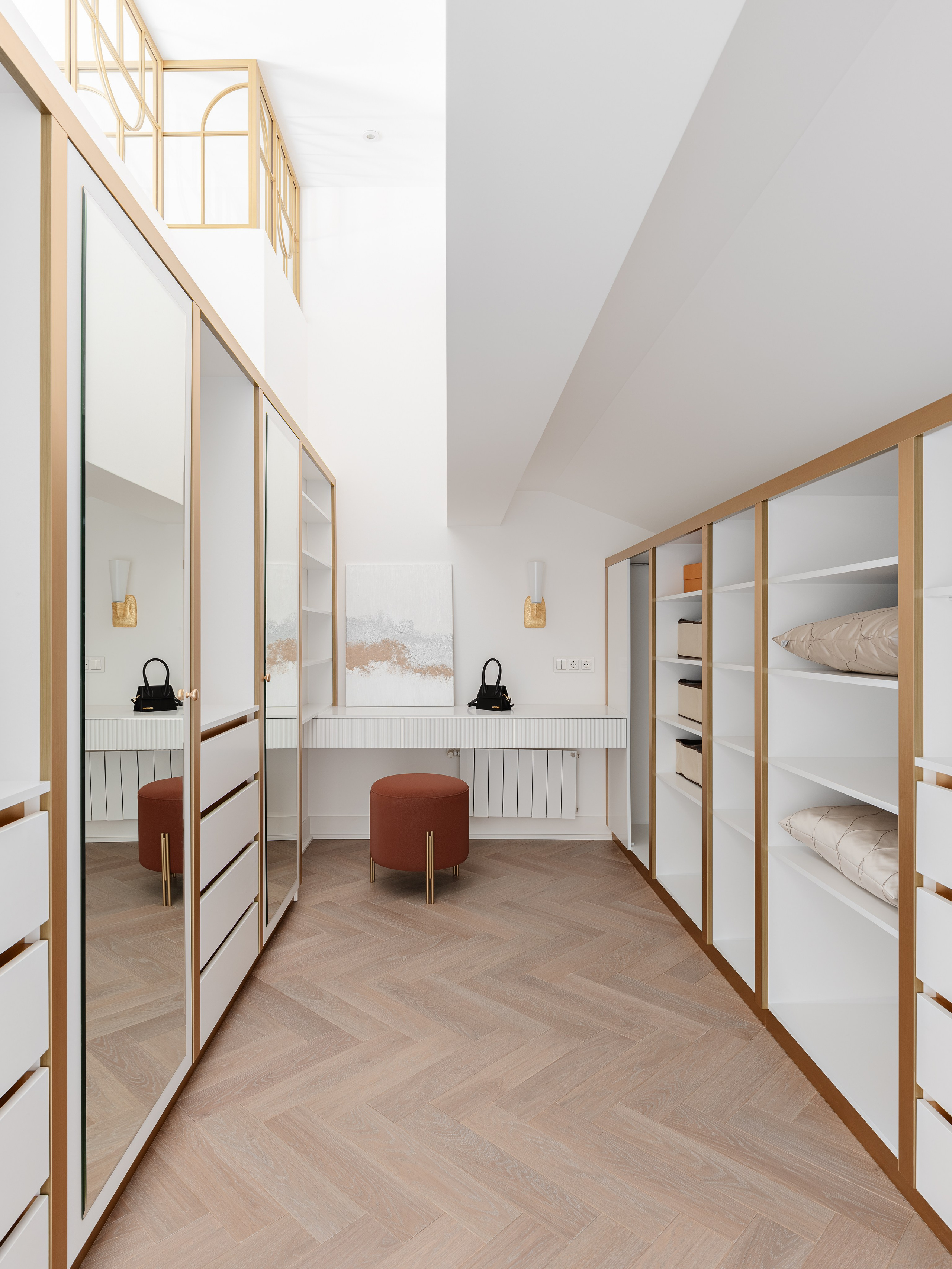 Светлая гардеробная комната с белыми встроенными шкафами, золотыми акцентами и большим зеркалом, паркет ёлочкой, пуф терракотового оттенка и мягкое освещение, интерьер от дизайнера Василиссы Бачевой, стилист Наталья Якушева, фото Сергей Денисенко.