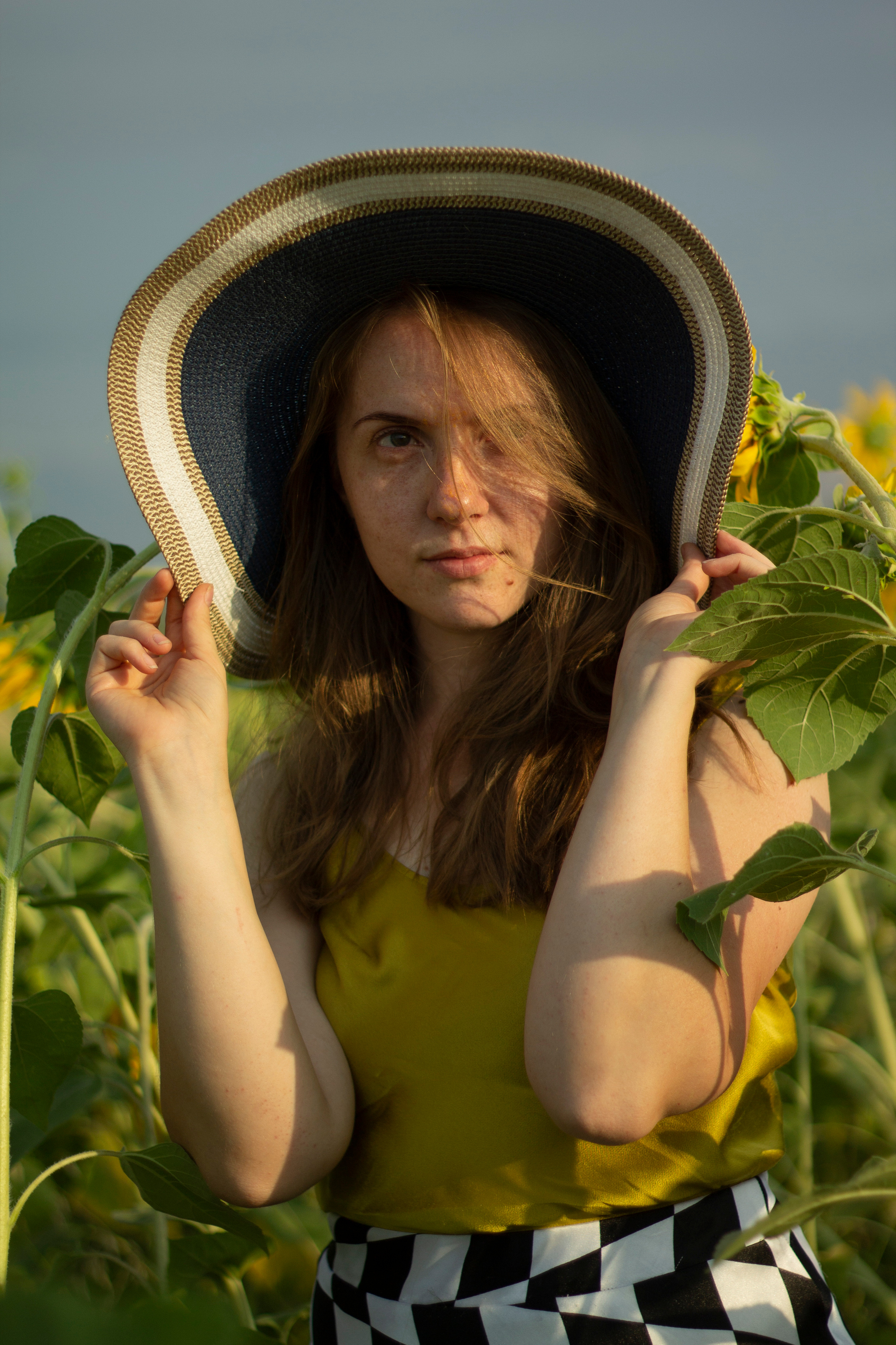 Lady in hat on the Helianthus field holding her hat