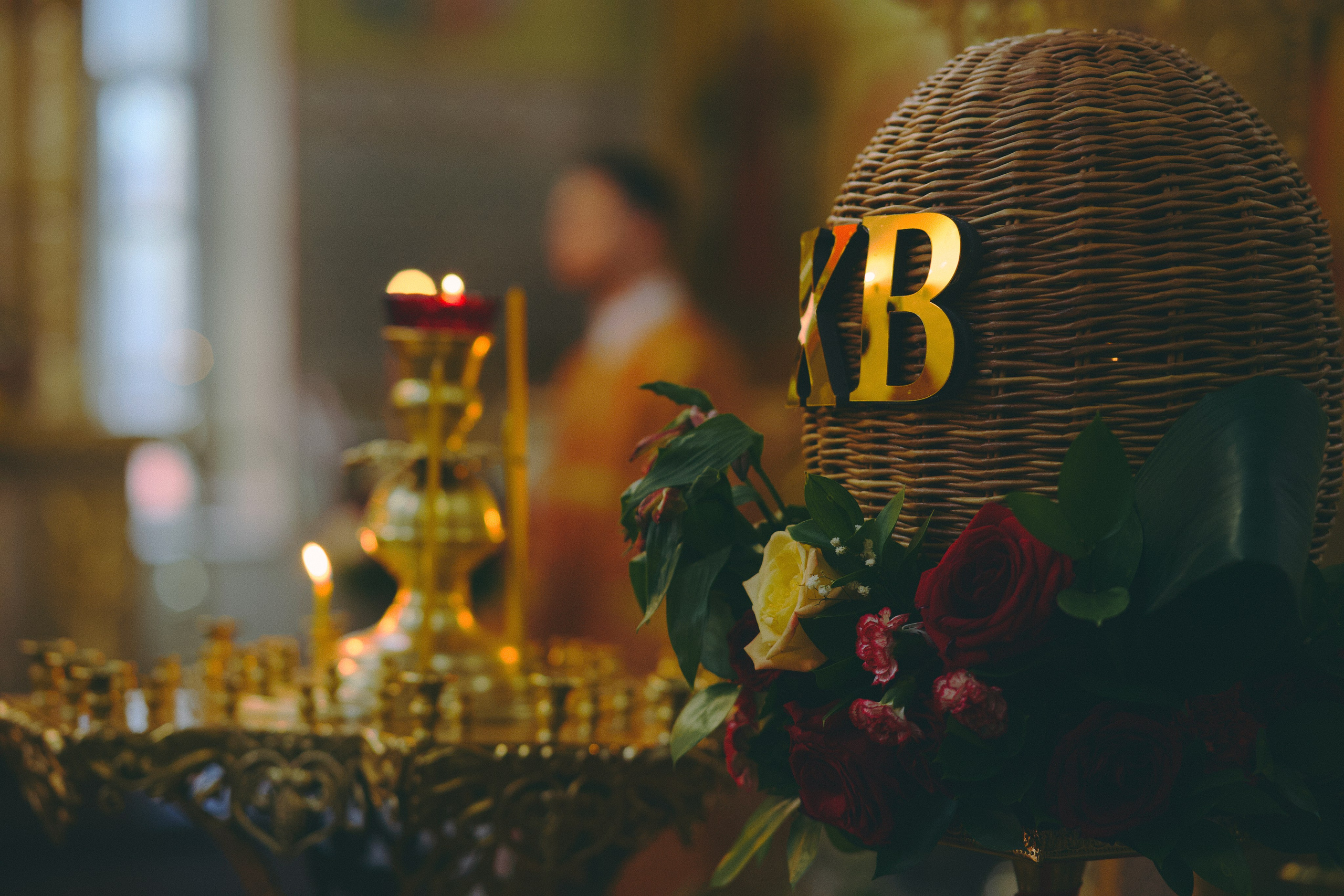 Пасхальная корзина с золотыми буквами «ХВ» (Христос Воскрес), украшенная живыми розами и зеленью. На заднем плане горящие свечи и иконы.