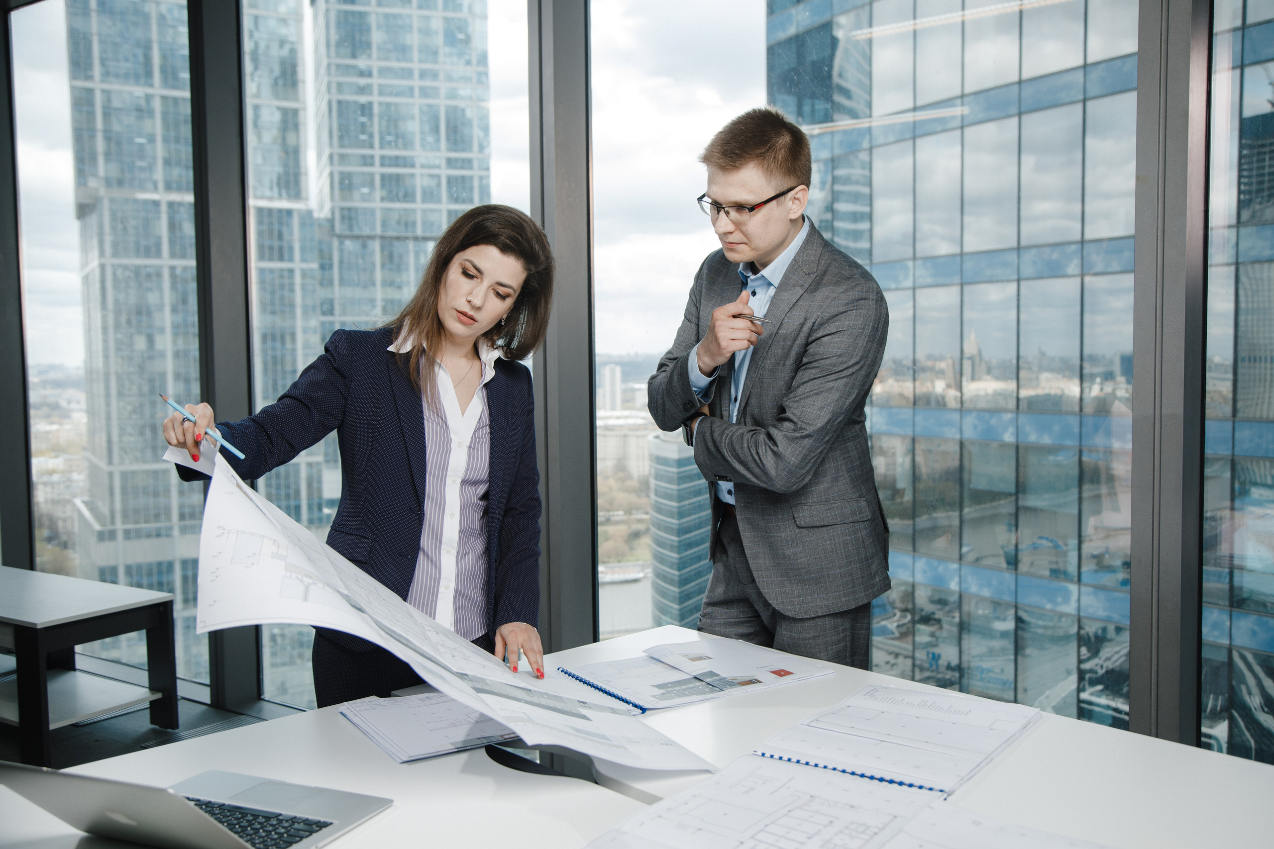 Два коллеги обсуждают рабочий вопрос в офисе на фоне Москва-Сити.