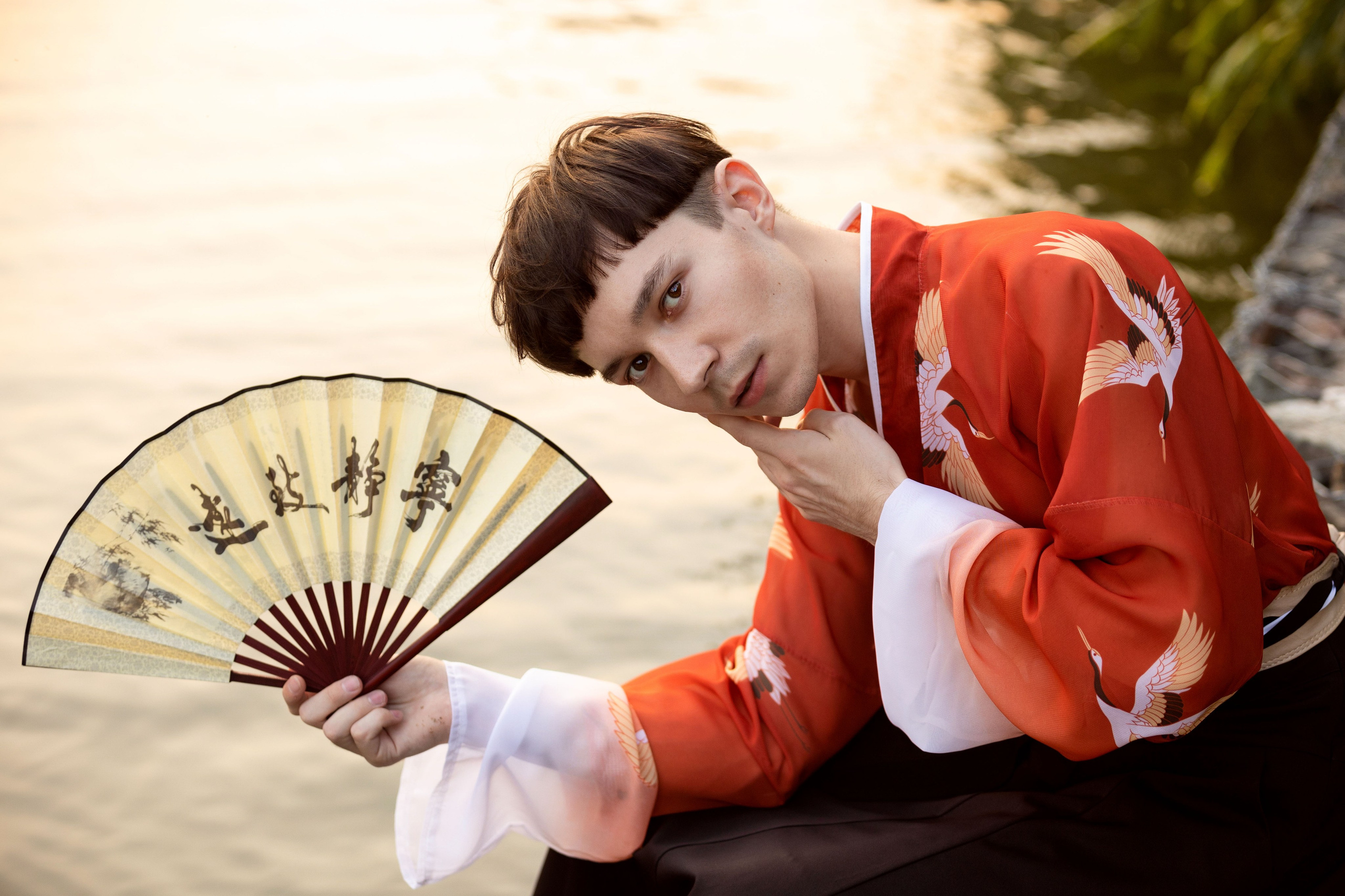Мужчина в красном кимоно с веером наклонился над водой.