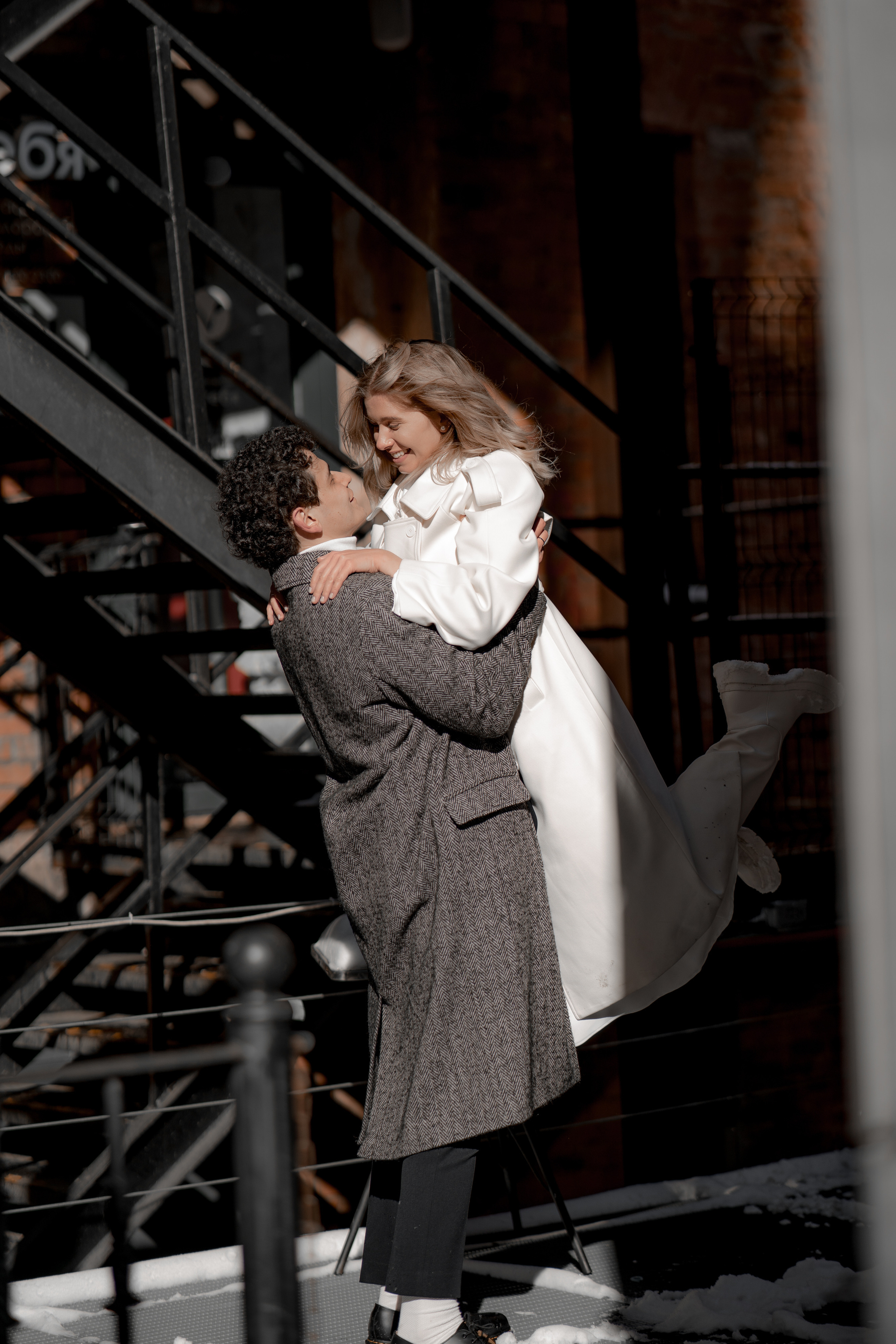 Молодой человек и девушка в пальто обнимаются в Бергольдц центре в Санкт-Петербурге.