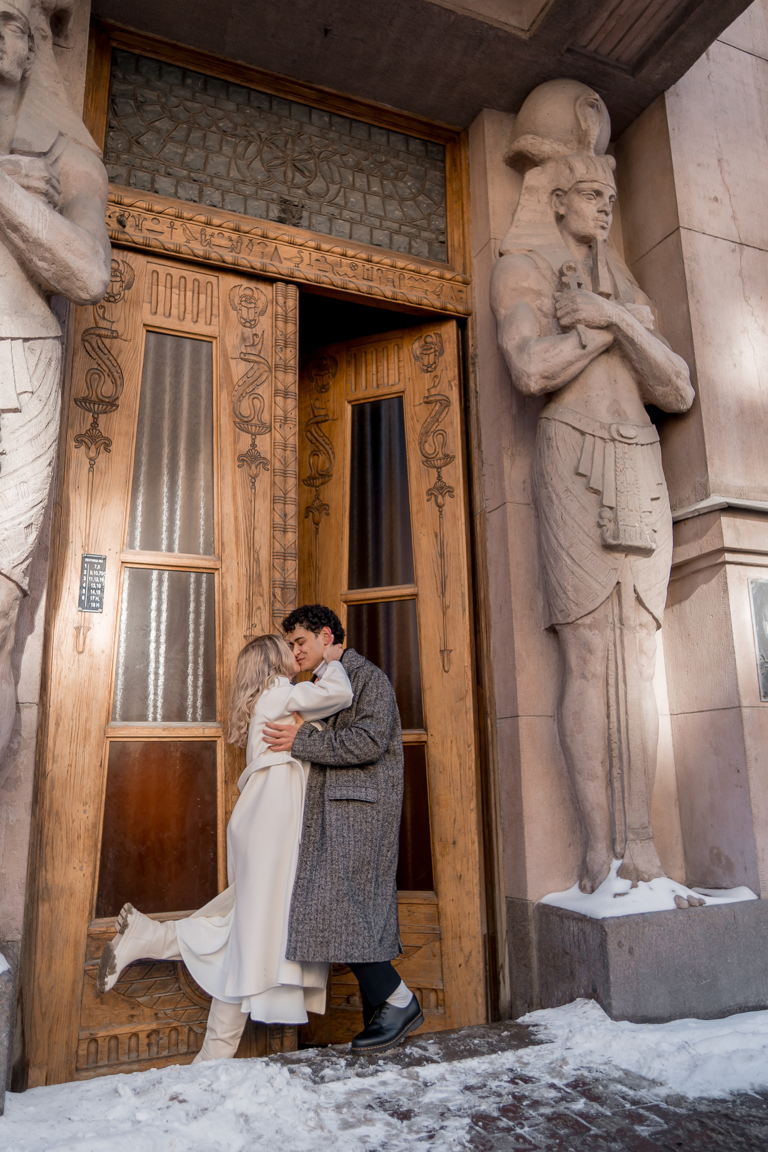 Влюбленная пара в зимних пальто обнимается у красивых дверей зимой в Санкт-Петербурге