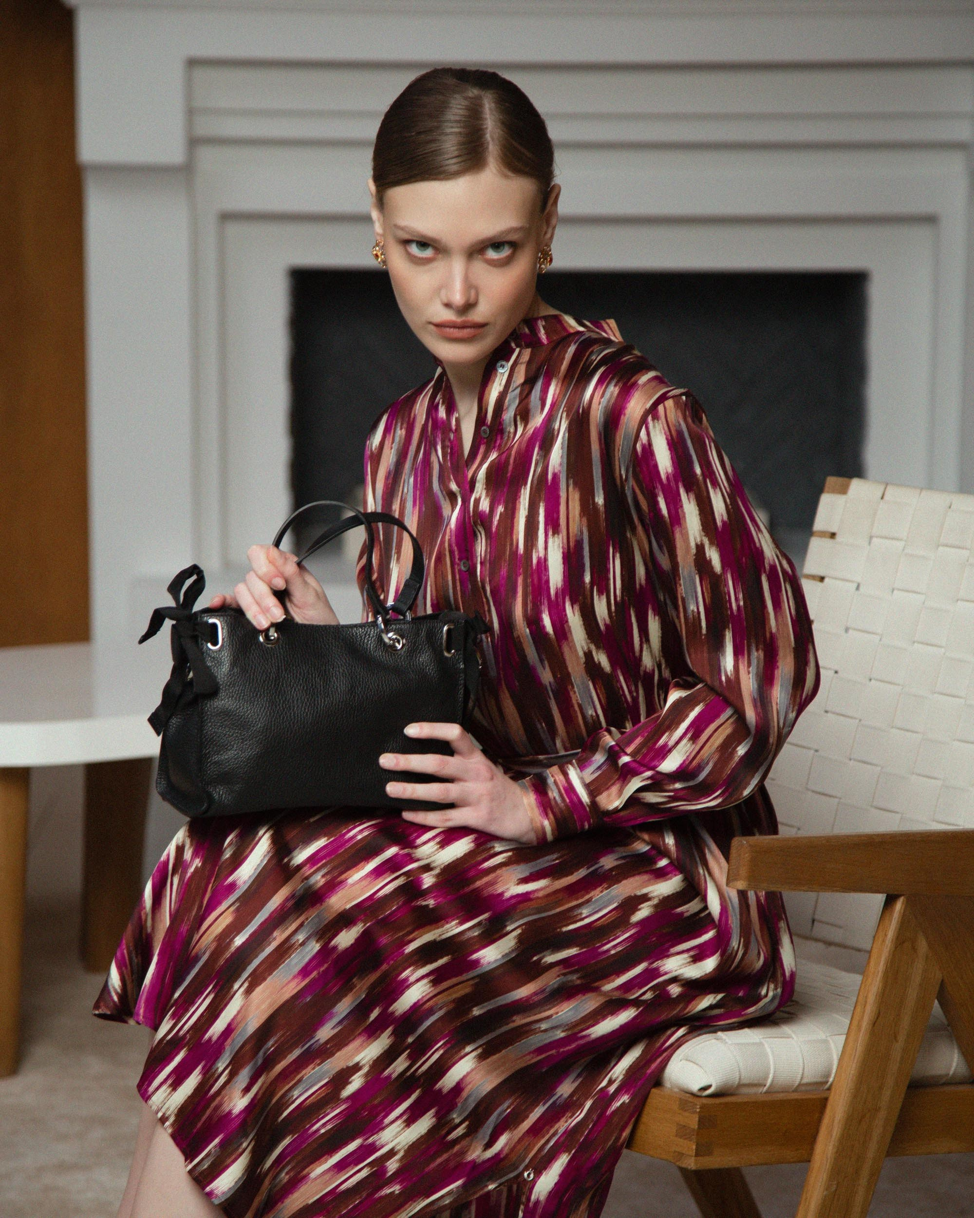 Девушка в  ярком платье сидит с черной сумкой на коленях