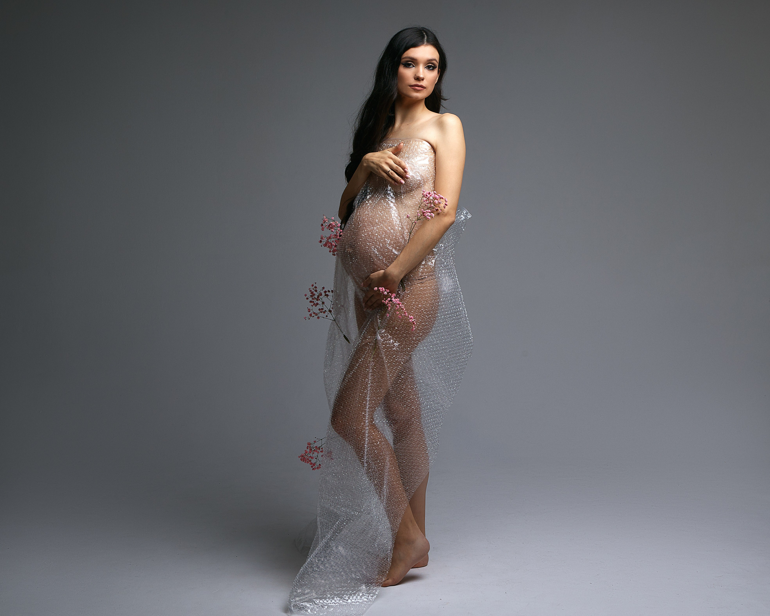 Беременная девушка в фотостудии в пленке и цветах