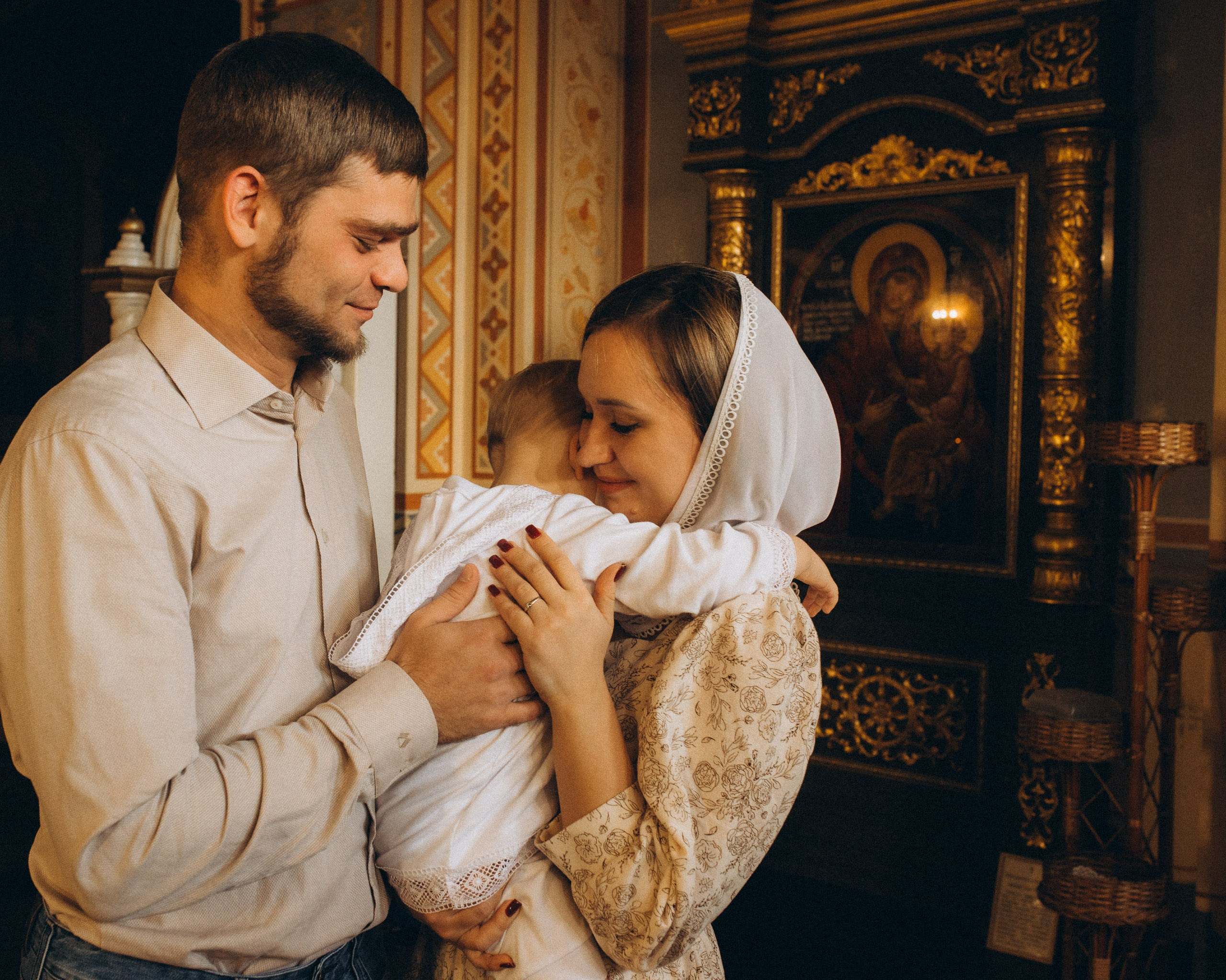 Фотосъемка крещения в Новосибирске — нежные объятия родителей и ребенка в церковном интерьере