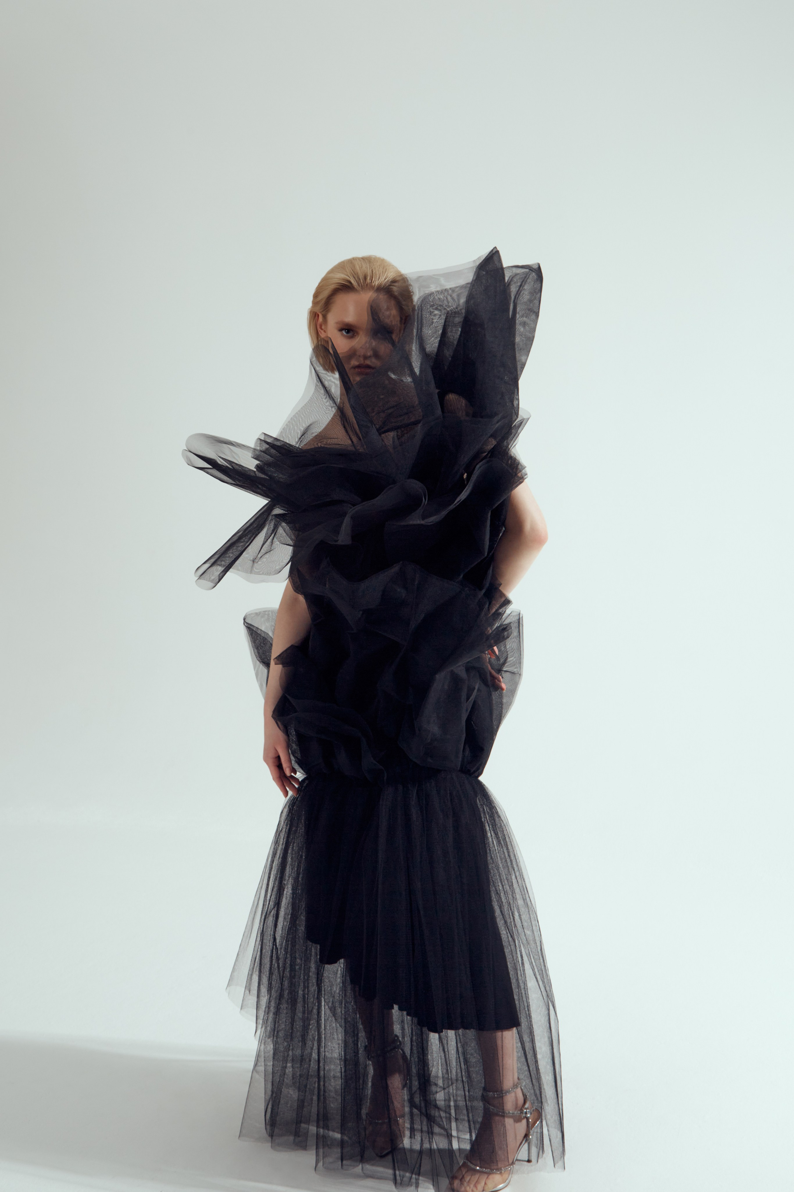 Девушка стоит в платье, состоящем из прозрачной черной сетки
