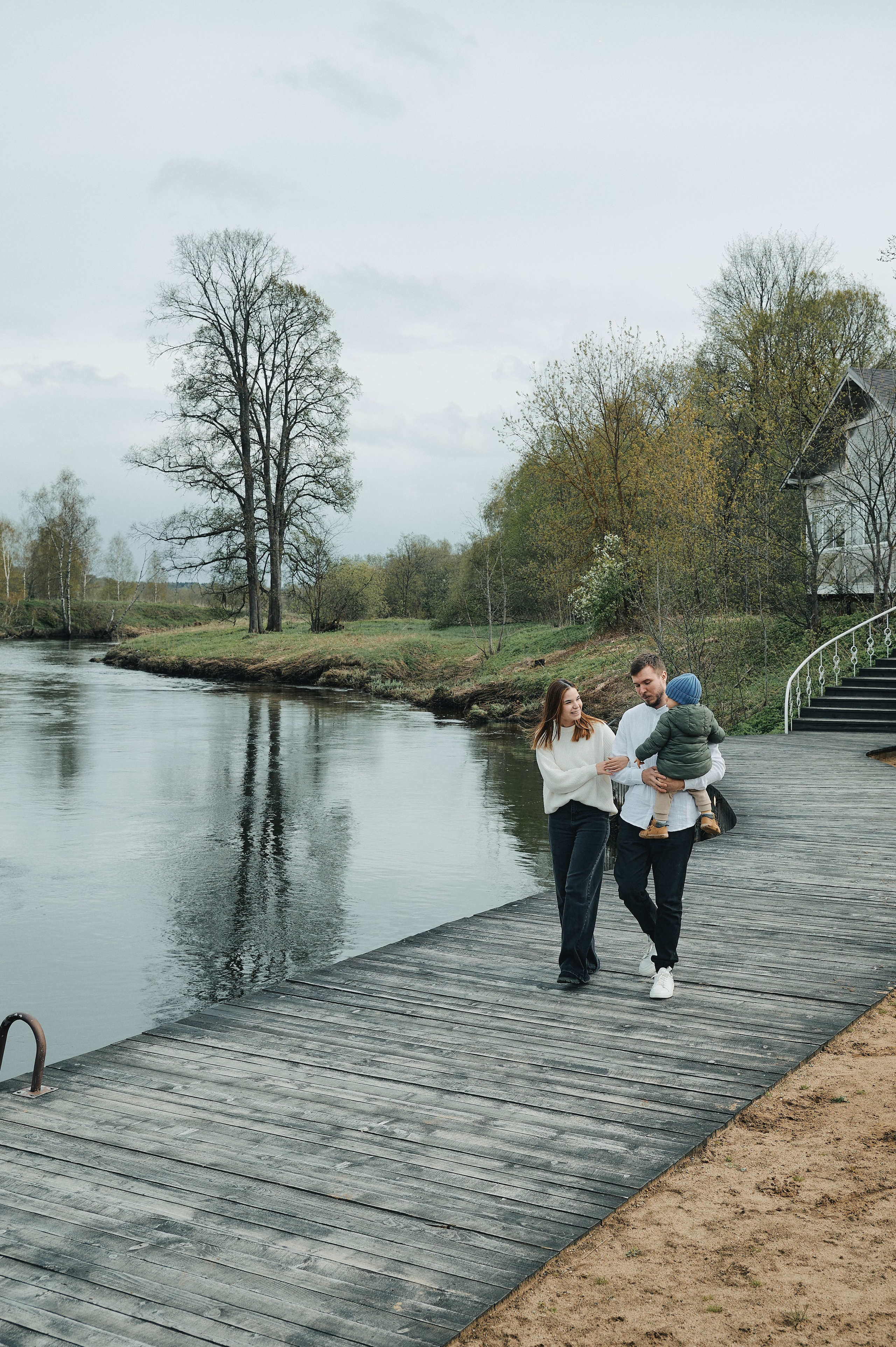 семья гуляет по деревянному настилу у реки, папа несёт ребёнка
