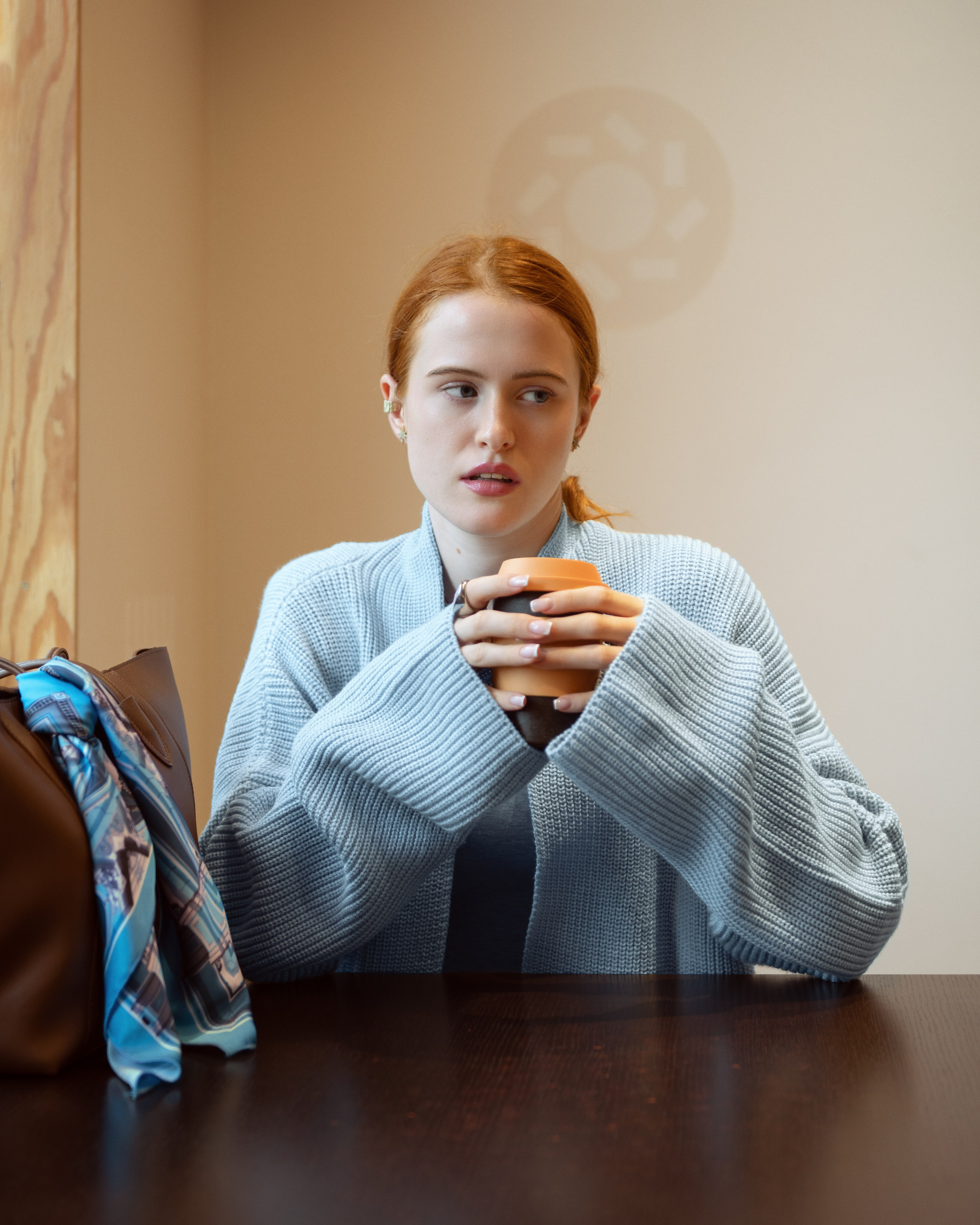 Красивая рыжеволосая девушка в голубом кардигане пьет кофе в кофейне