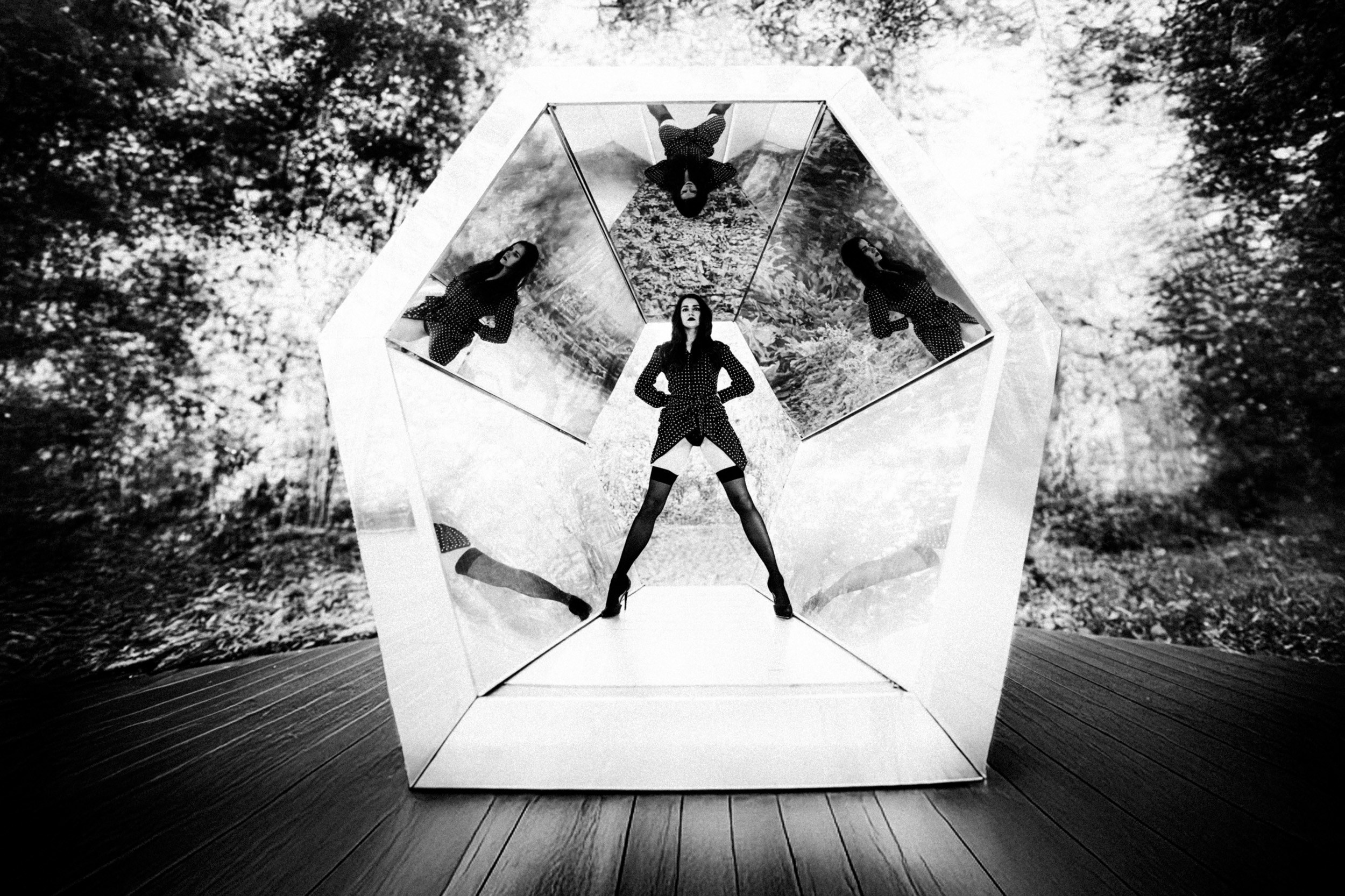 Чёрно-белая фотография женщины в платье в горошек и чулках в зеркальной инсталляции на фоне леса