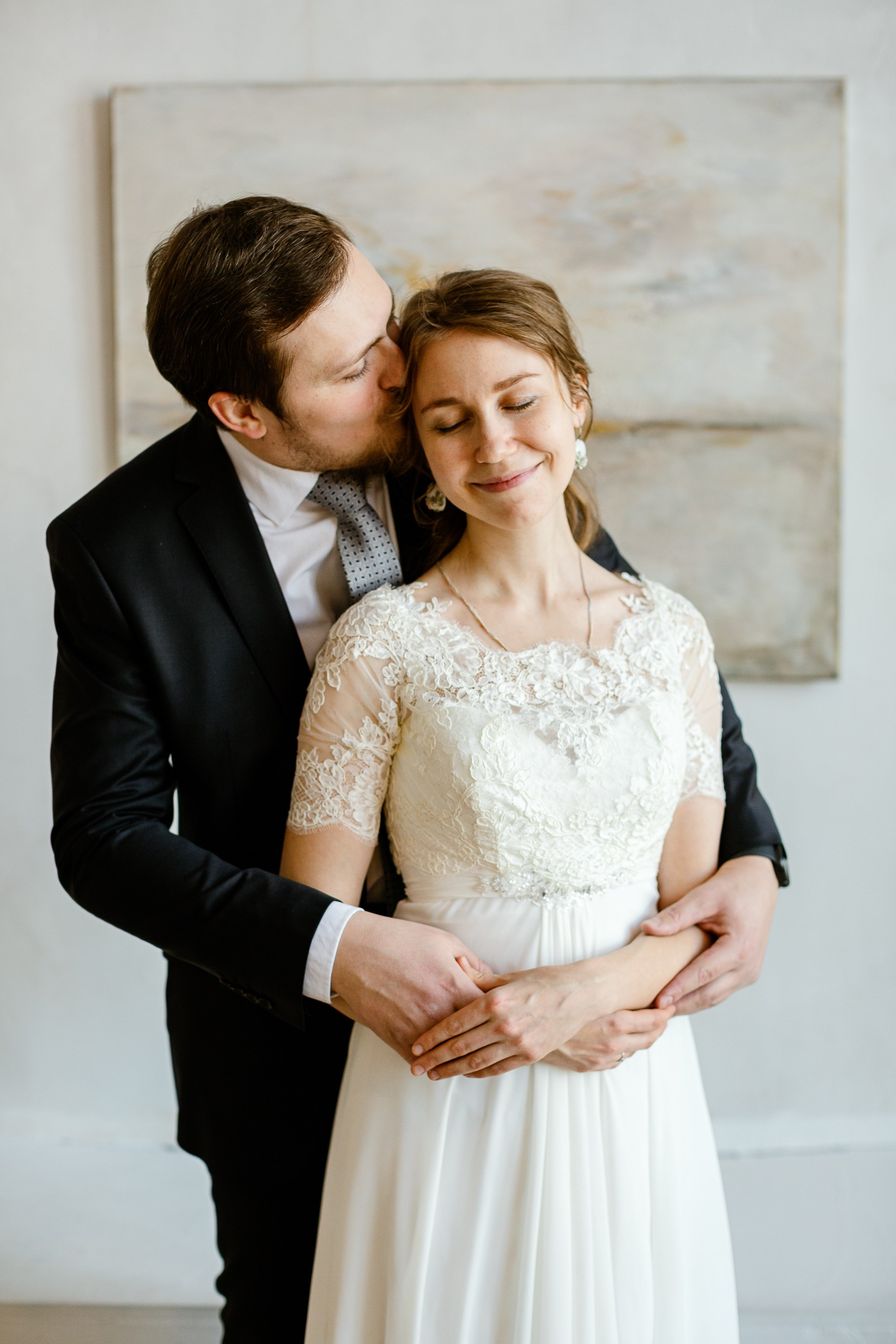 Жених и невеста в праздничной фотостудии. Жених в костюме, невеста в красивом белом платье. На фоне картина.