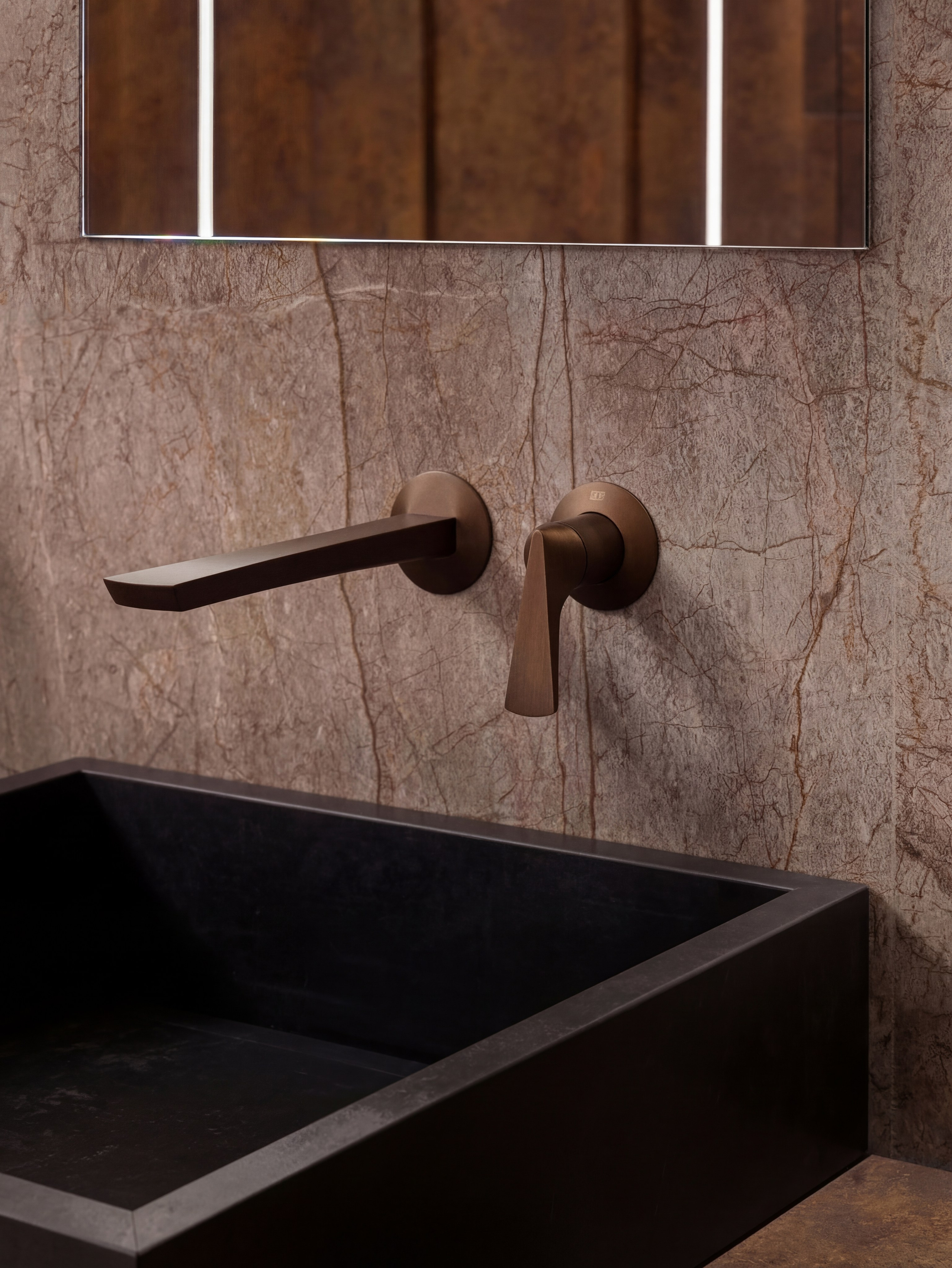Детальный вид зоны умывания от Валерии Котович: встроенный бронзовый смеситель, черная матовая раковина и стена из натурального камня с подсветкой в интерьере мастер-ванной.