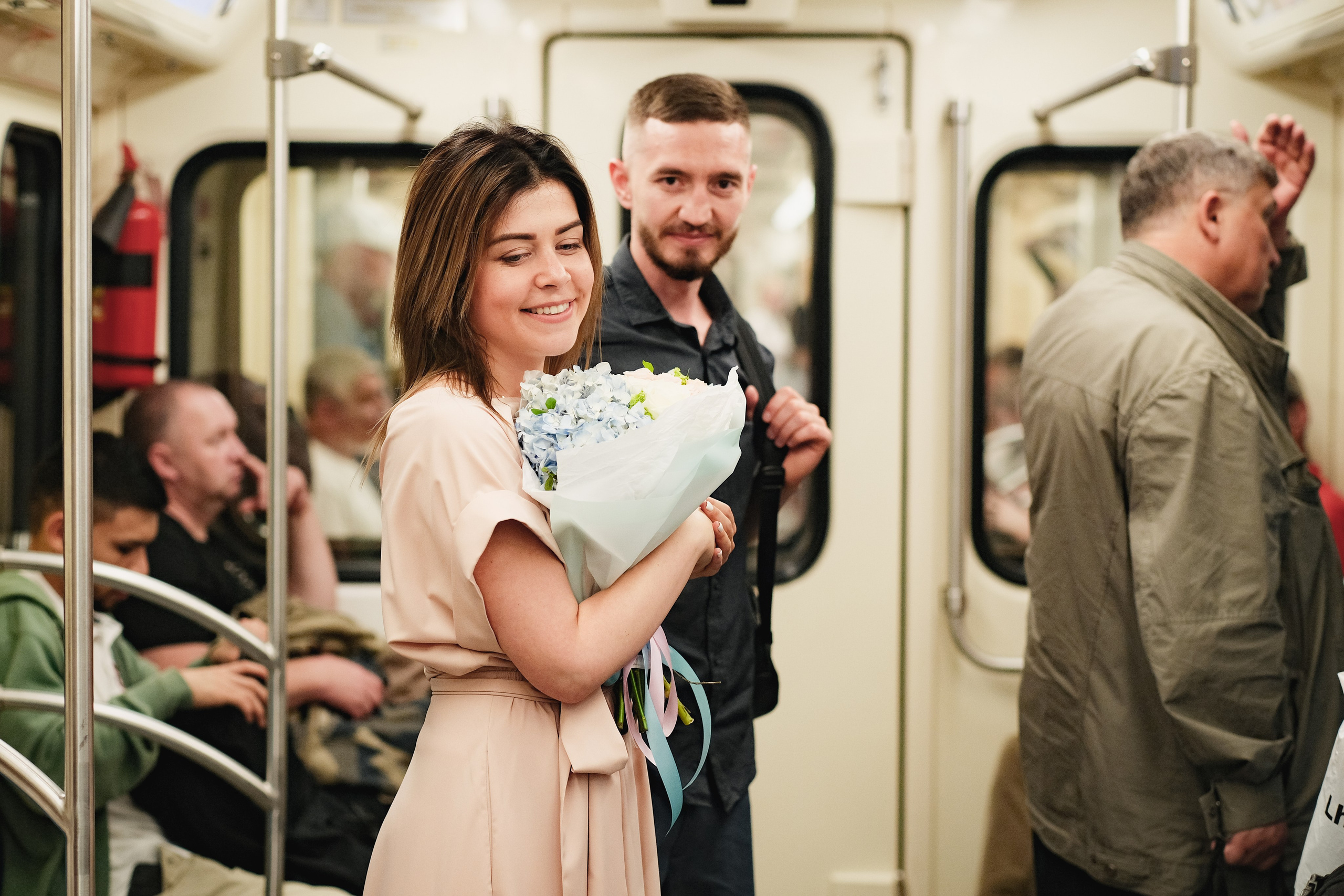 Девушка с букетом в вагоне метро, рядом парень.
