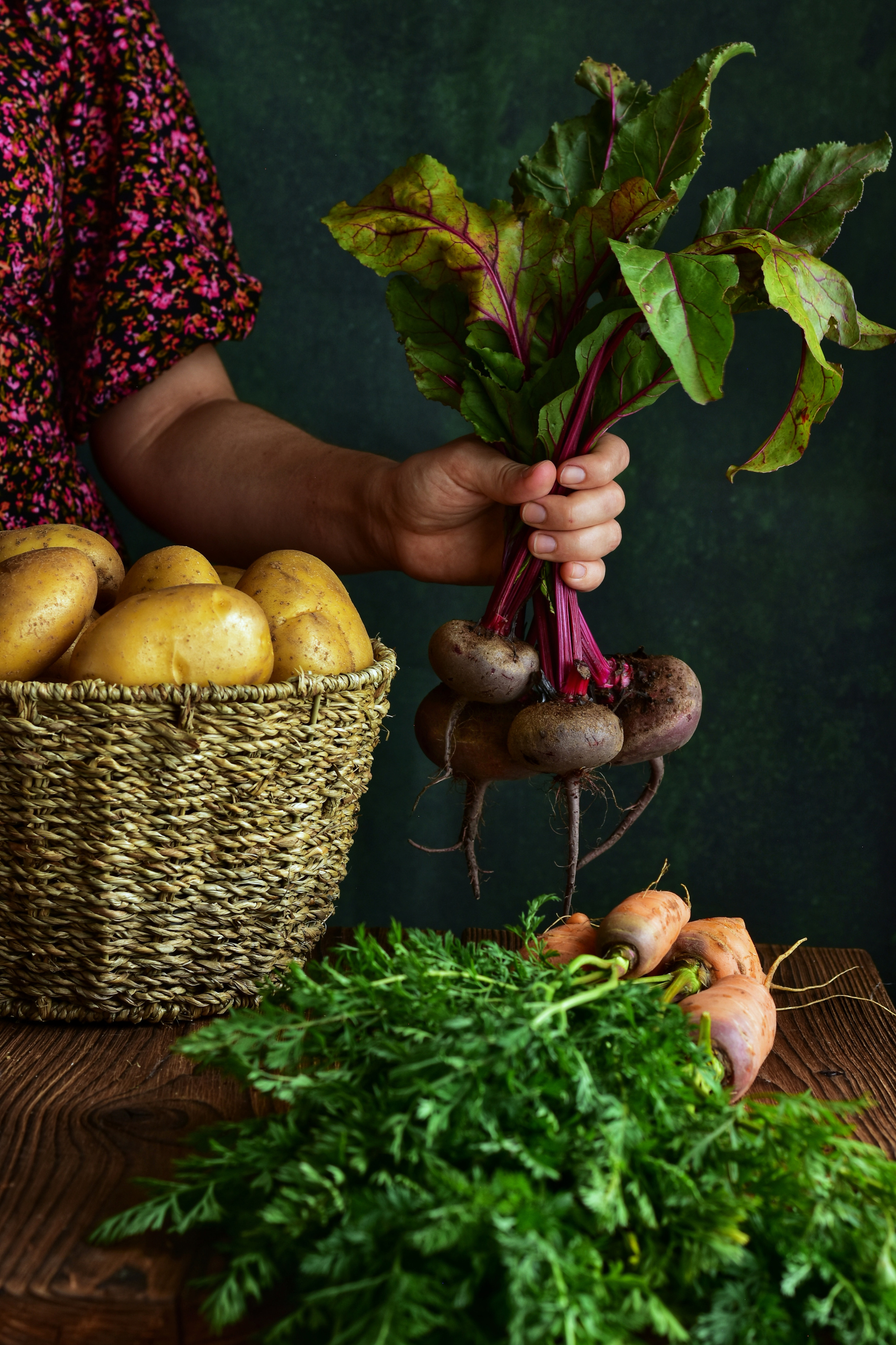 женская рука, держащая связку редиски перед корзиной картошки и связкой моркови