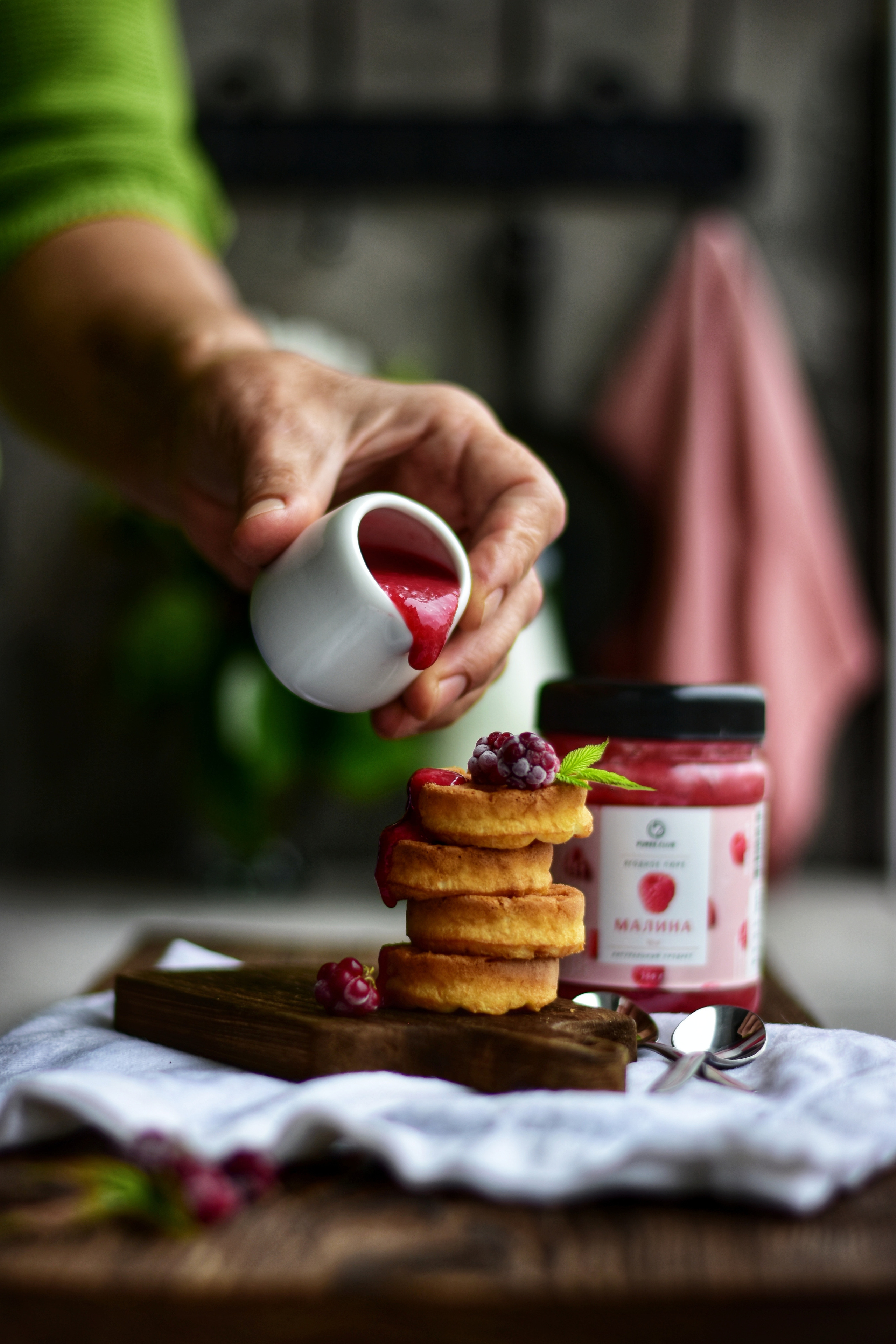 женская рука наливает варенье на стопку блинов