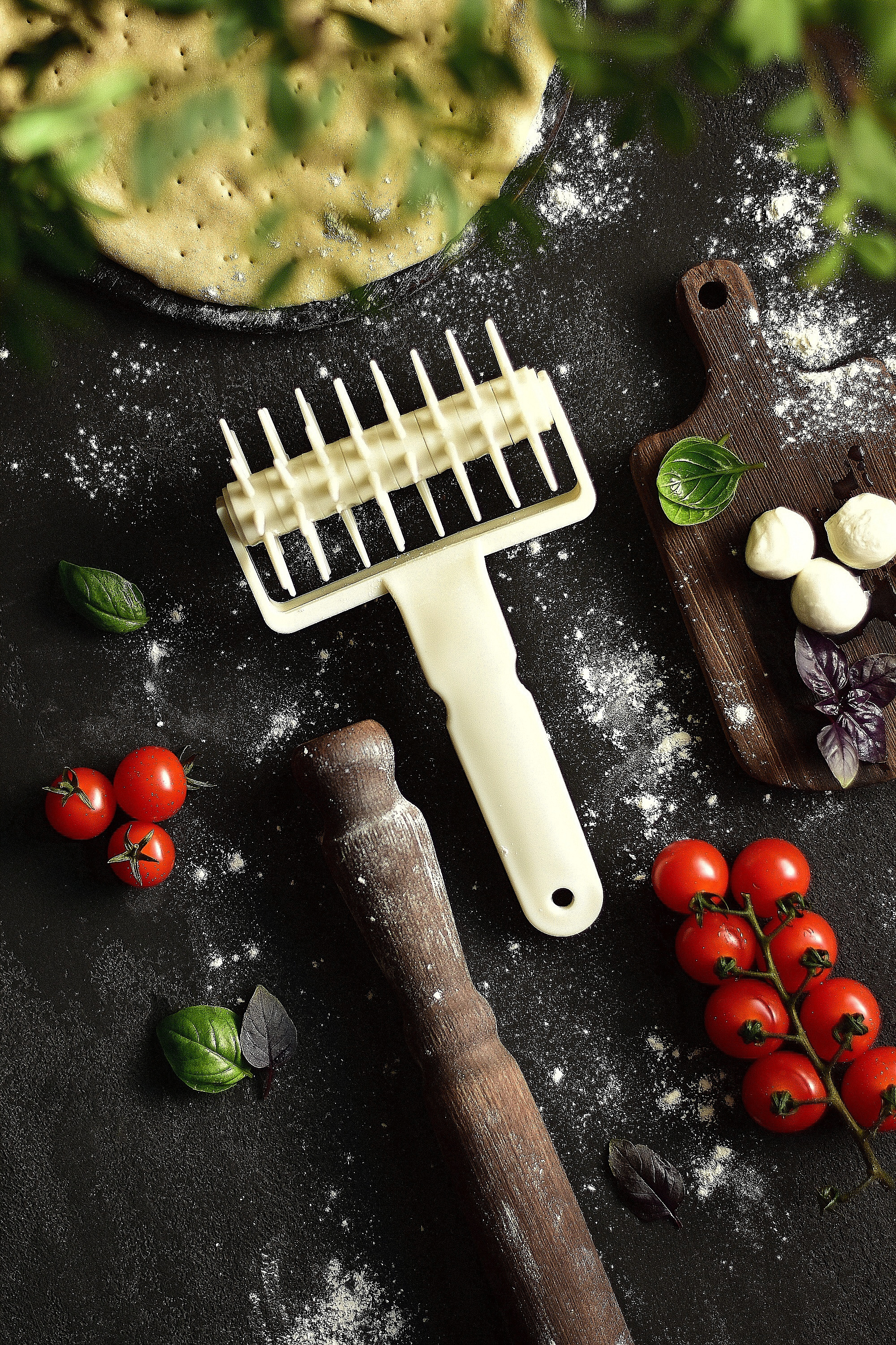 ролик для теста рядом с кучей помидоров и тестом на деревянном столе