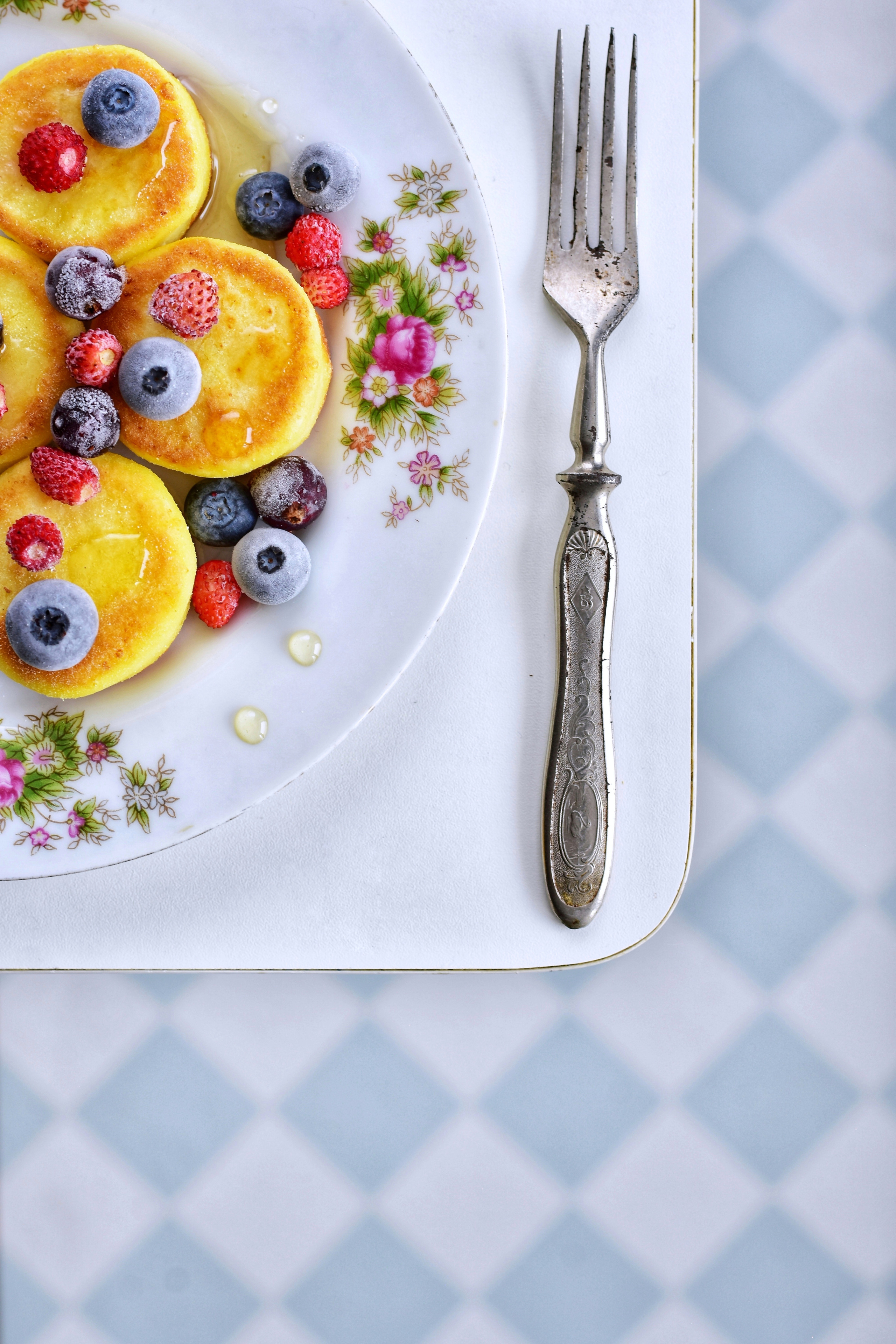 вилка на белой тарелке с блинами и ягодами.