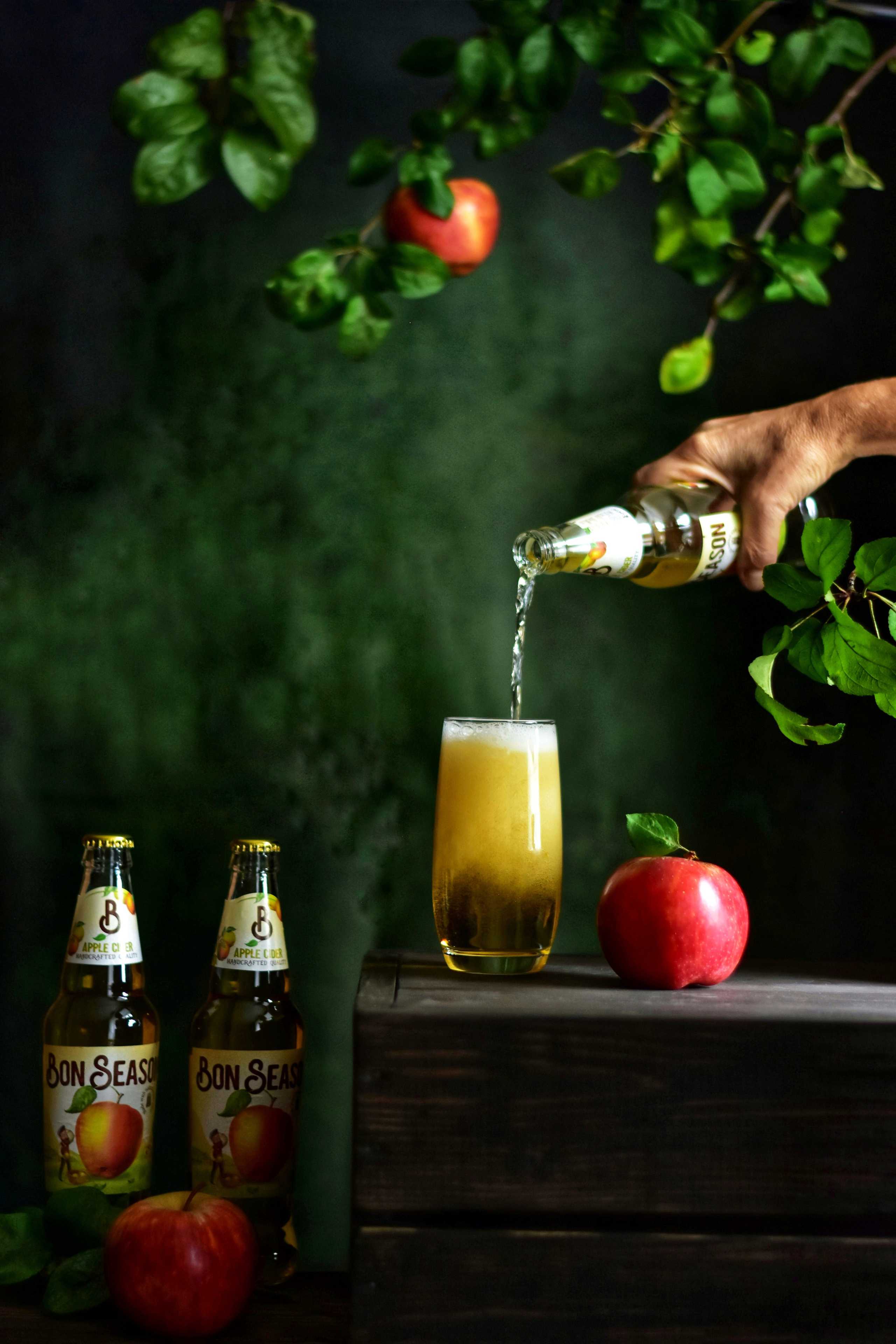 женская рука, наливающая сидр в стакан, окруженный яблоками
