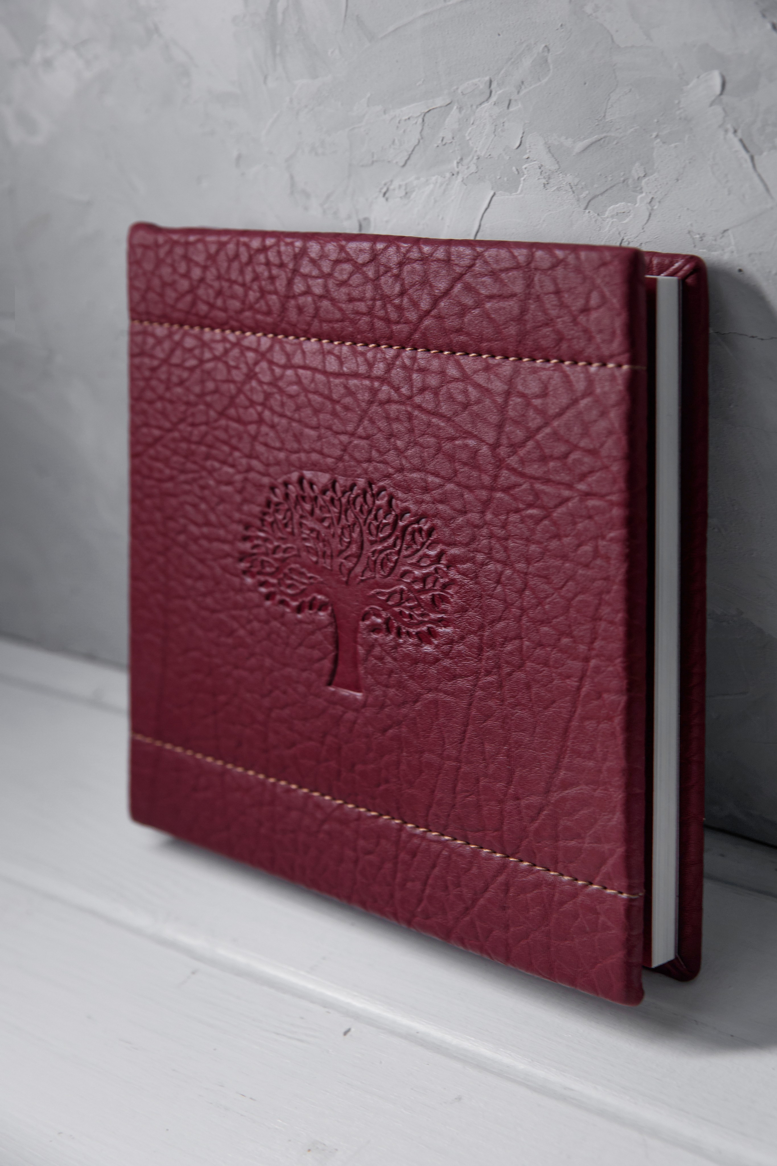 Фотокнига в темно-красном кожаном переплете с тиснением дерево и декоративной прошивкой.