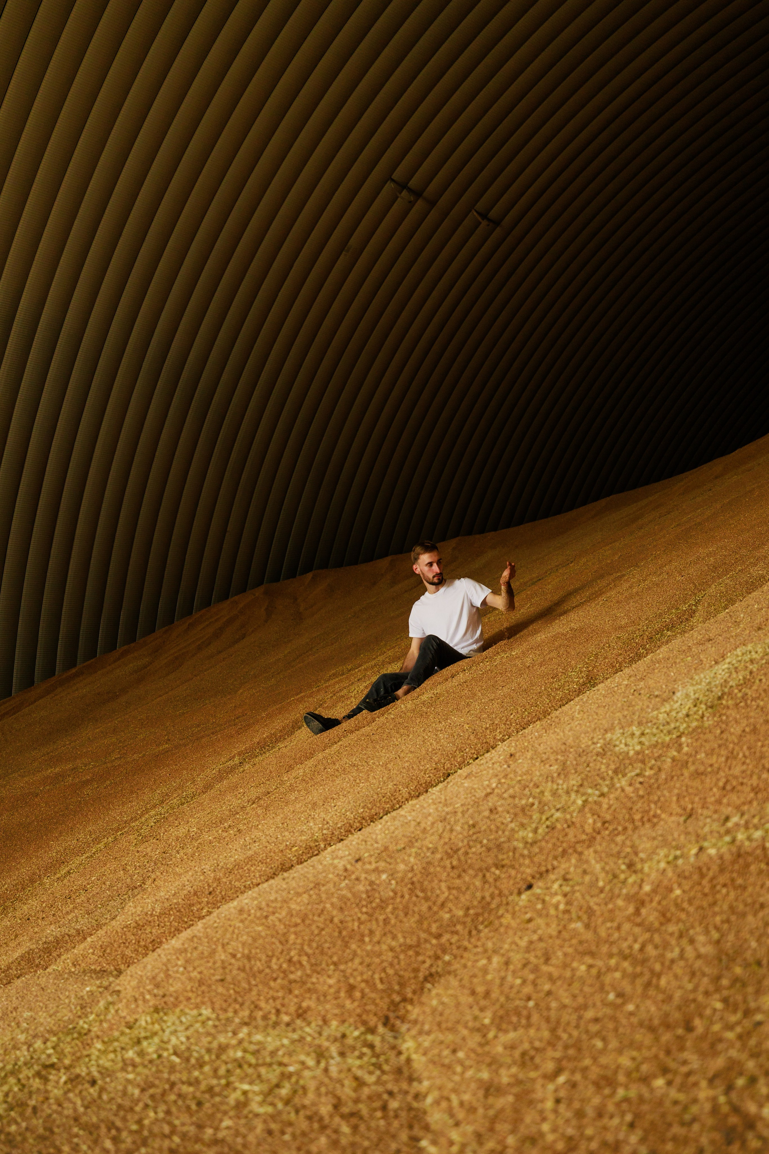 Мужчина на горе зерна внутри хранилища, тёплый свет, геометрия купола, Тавда, Илья Антропов