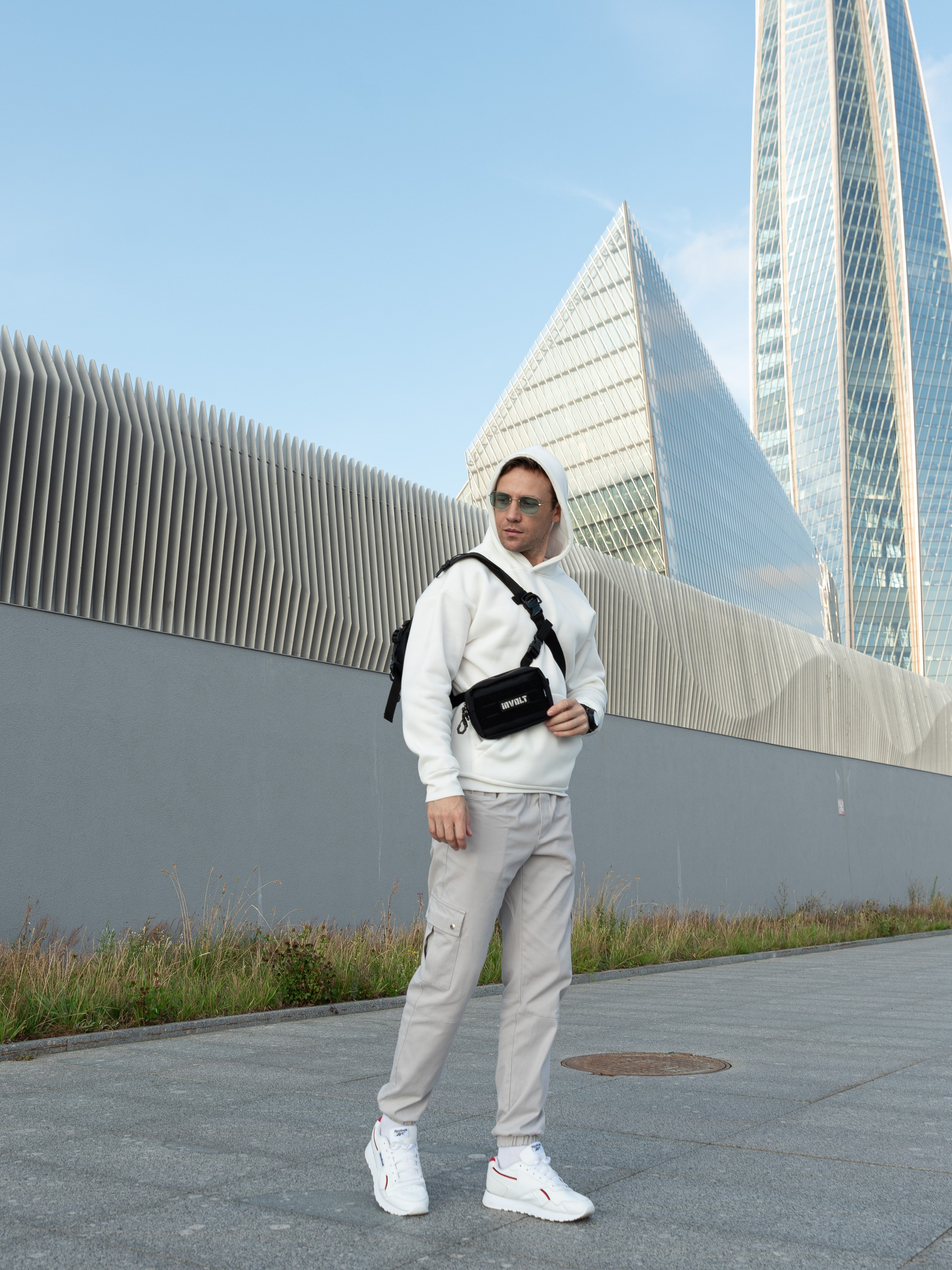 Мужчина в белой кофте с капюшоном и солнечных очках на фоне небоскребов