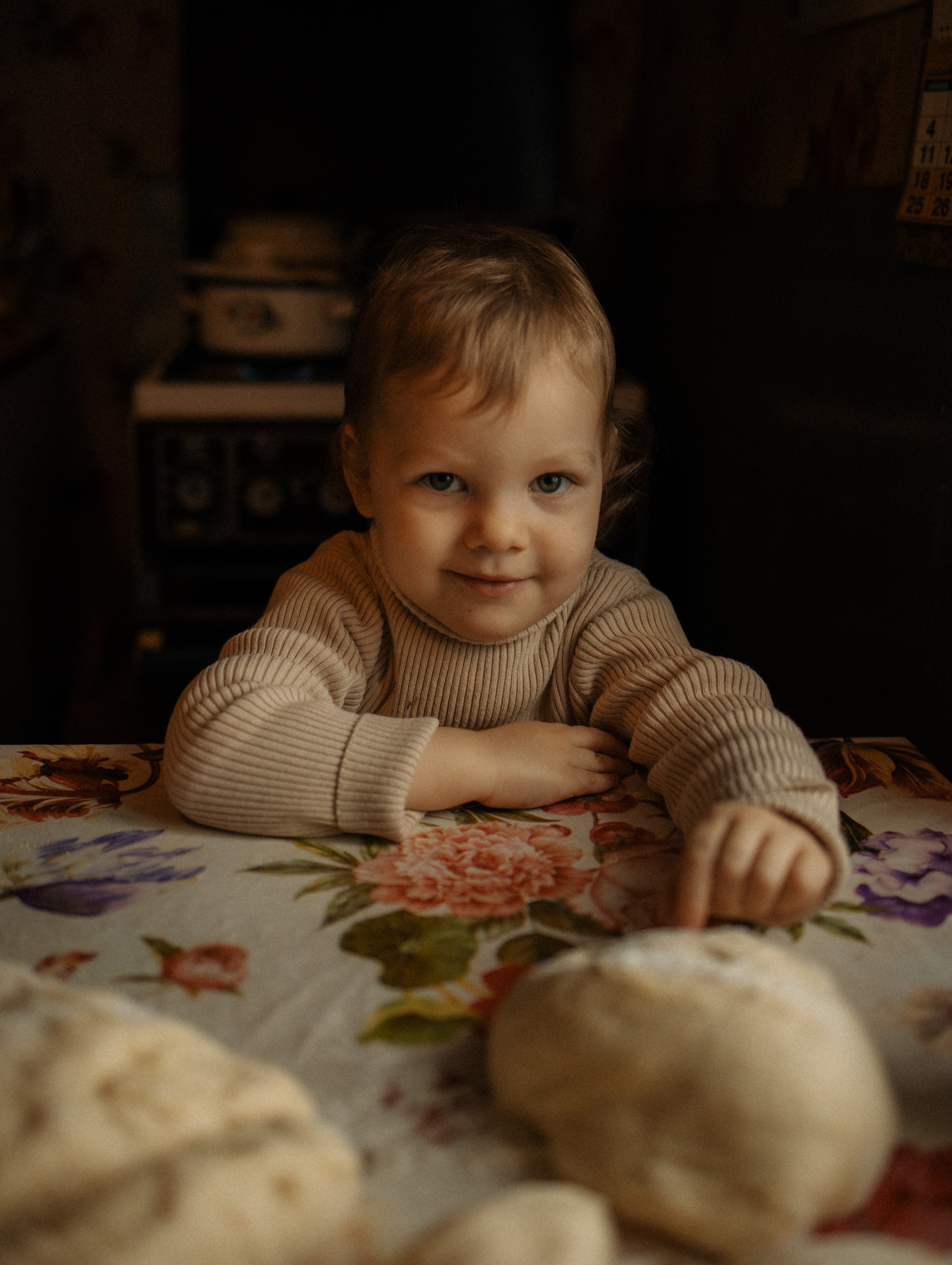 Милая маленькая девочка сидит за столом на кухне и смотрит в кадр