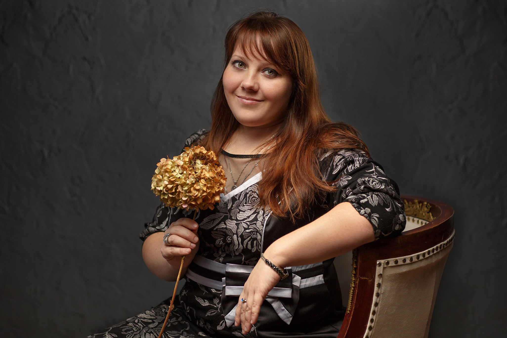 полная девушка в кресле с букетом сухих хризантем в фотостудии