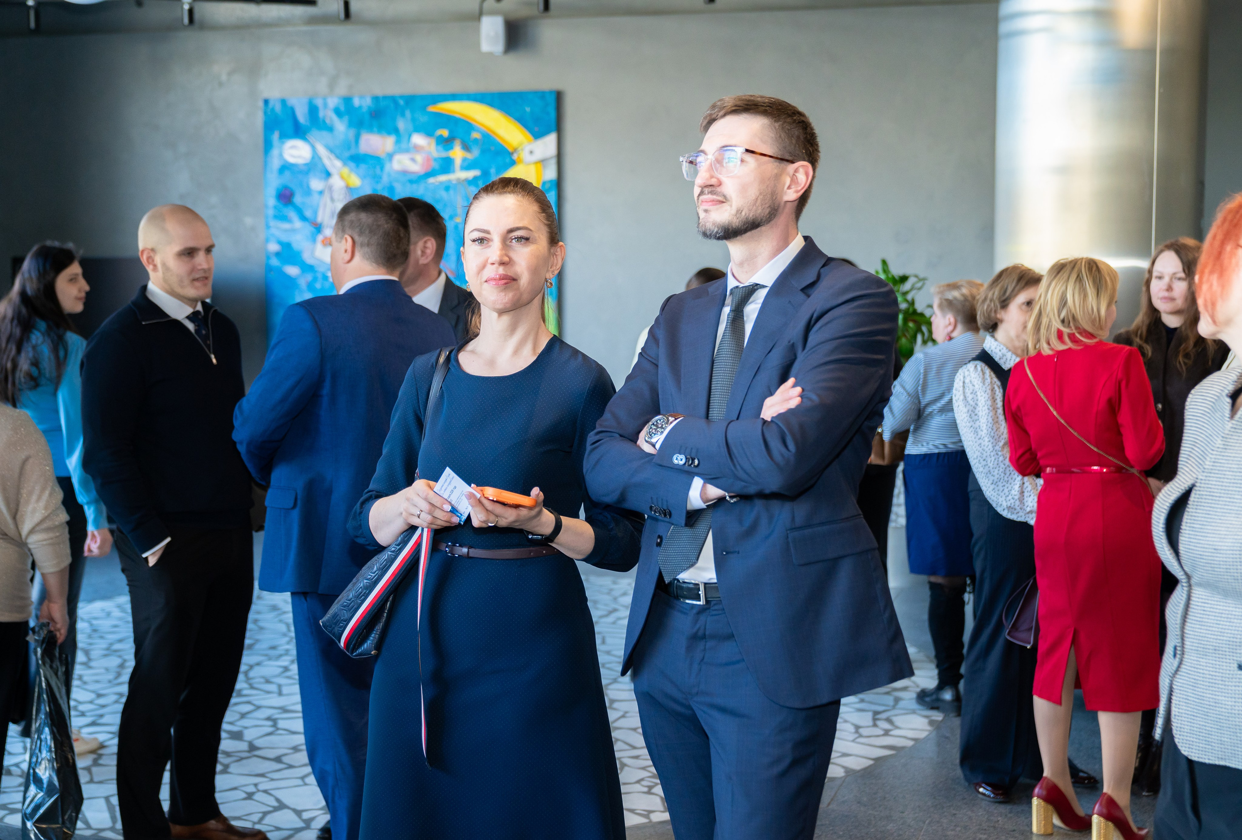 Гости мероприятия День местного самоуправления в Санкт-Петербурге. Мужчина в костюме и женщина в синем платье на выставочном пространстве. Фотограф Евгений Мальцев.