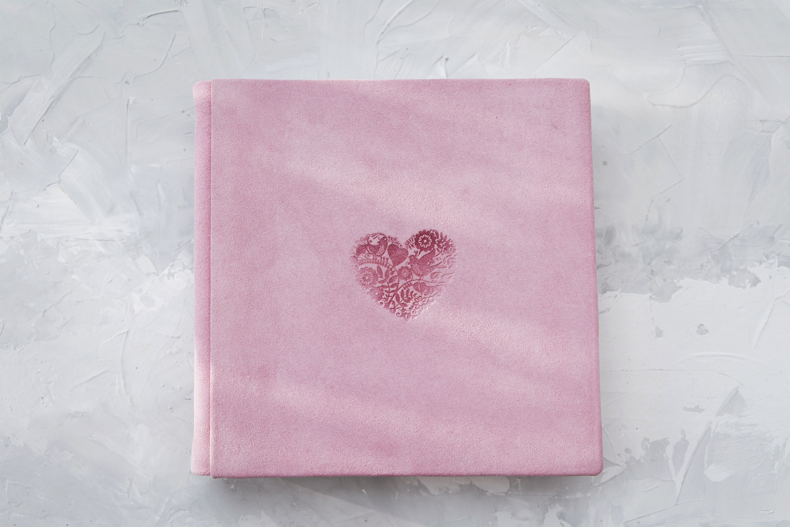 Квадратная фотокнига из розовой замши с тисненым декоративным сердцем по центру.