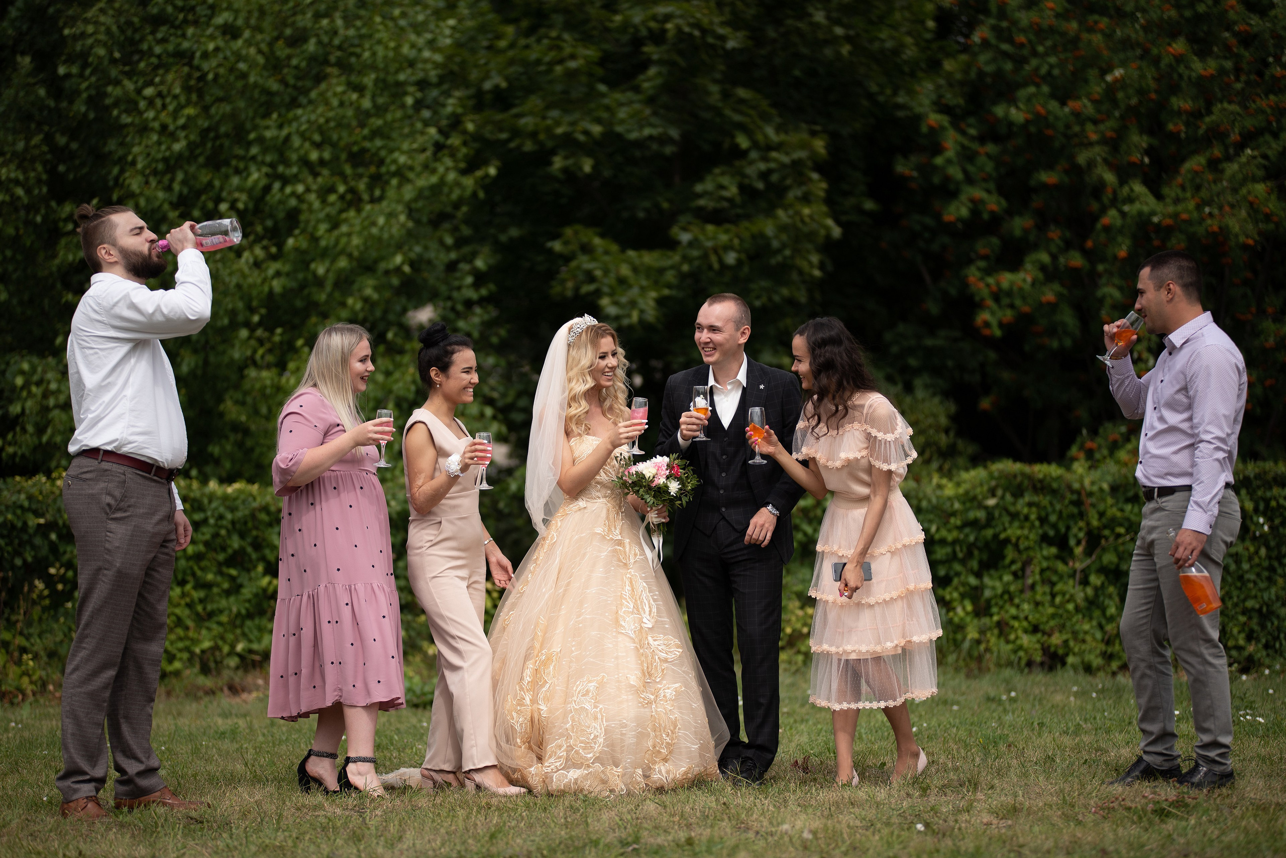 Групповой свадебный снимок, на котором гости веселятся, распивают шампанское, поздравляют молодоженов.