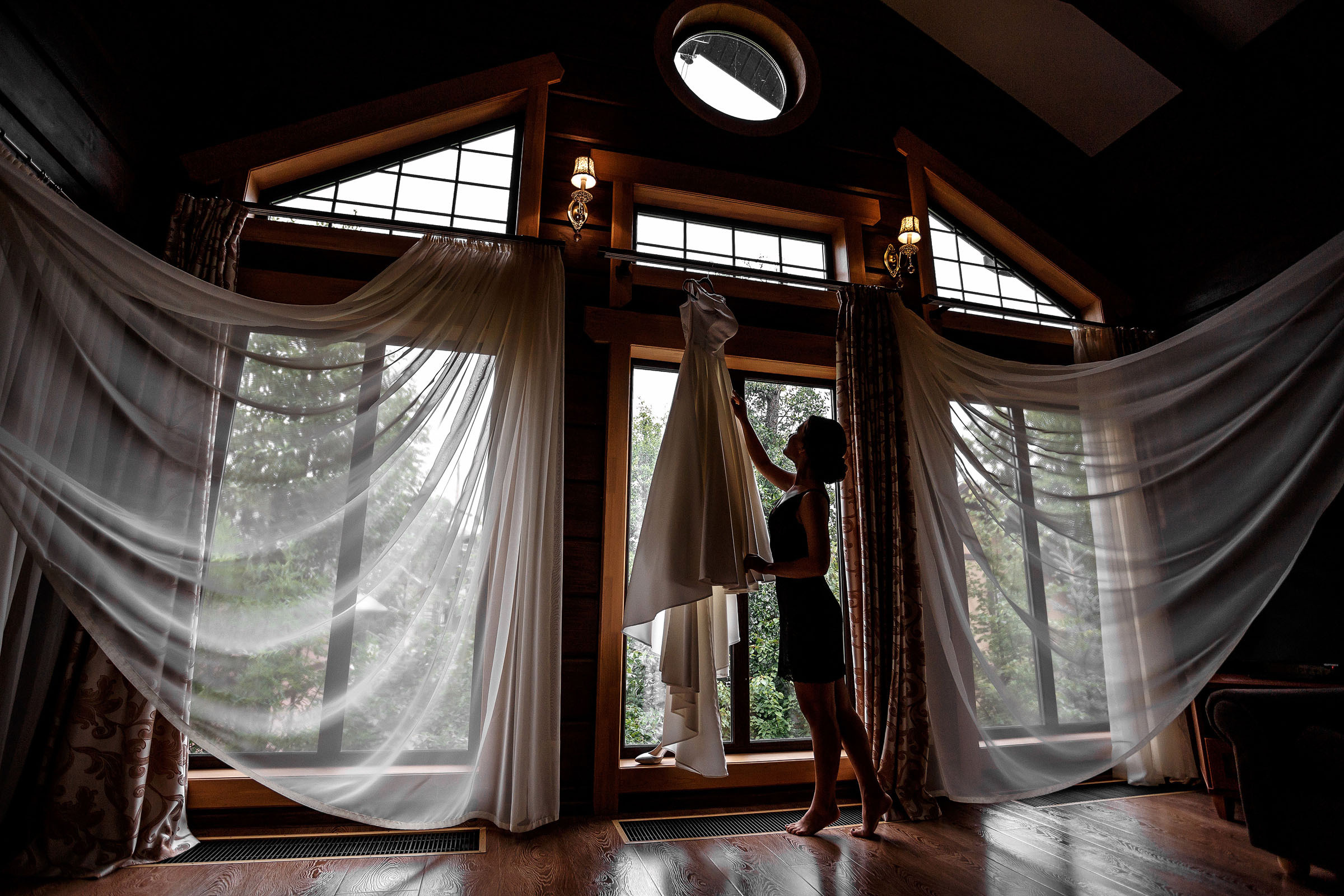 Невеста снимает свадебное платье на фоне красивых штор и окна 