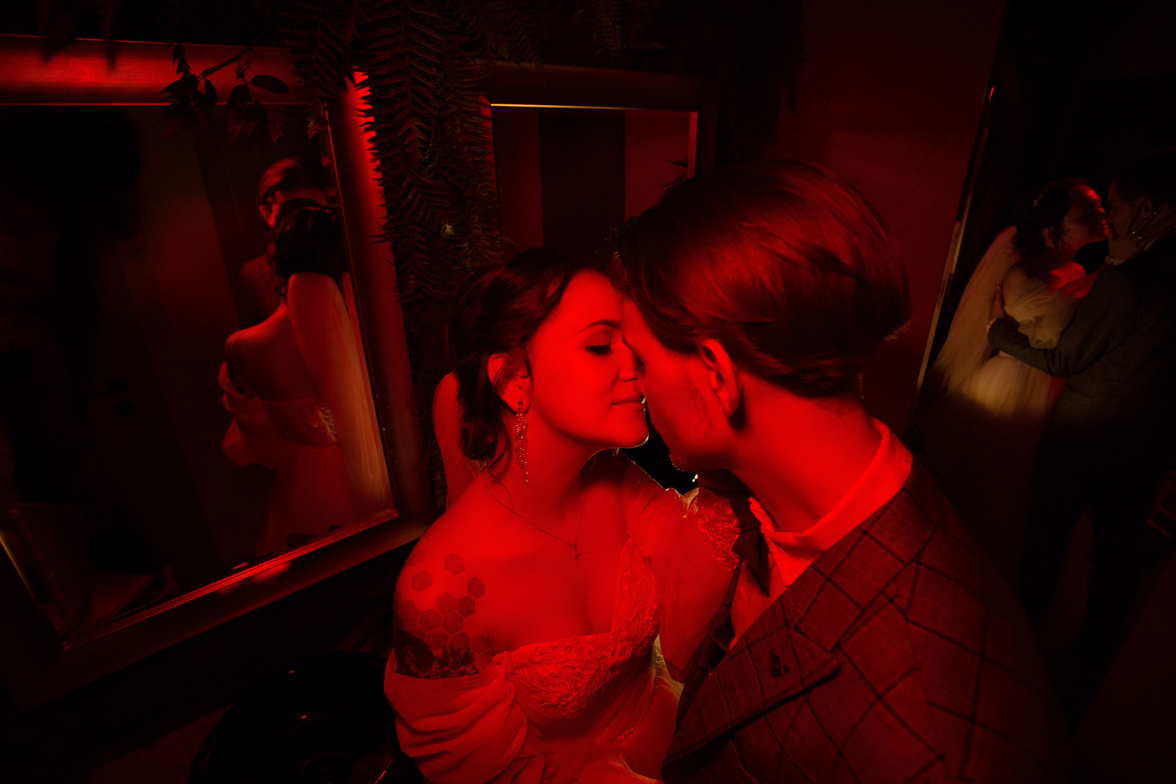 Невеста целует жениха в красном свете ламп. Свадебная фотография Андрея Куликова