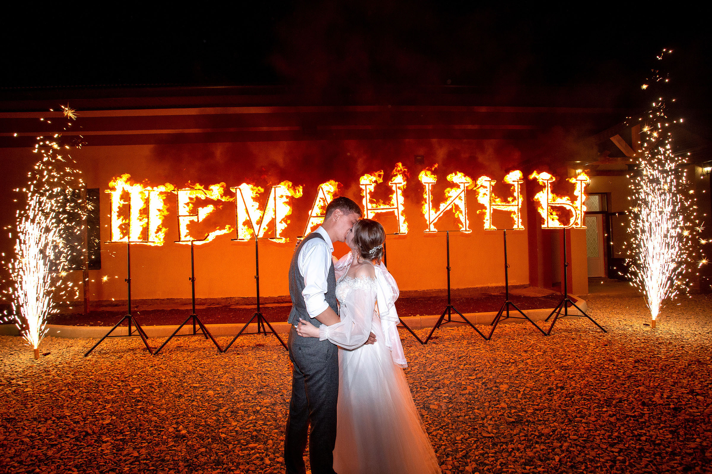 Жених и невеста целуются на фоне холодных фонтанов в темноте