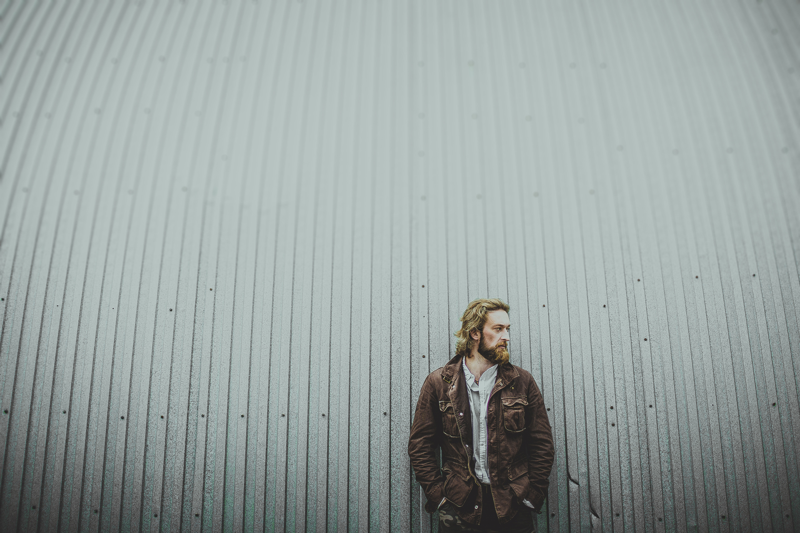 брутальный мужчина в рубашке и кожаной куртке на фоне ангара в профиль