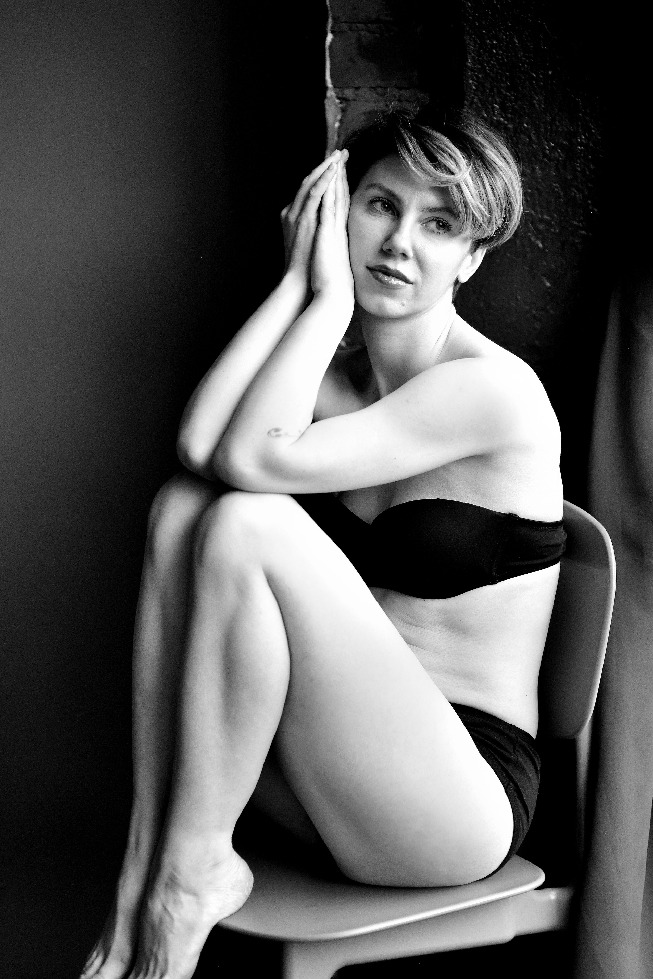 Девушка с идеальной фигурой в черном нижнем белье томно сидит на стуле.
