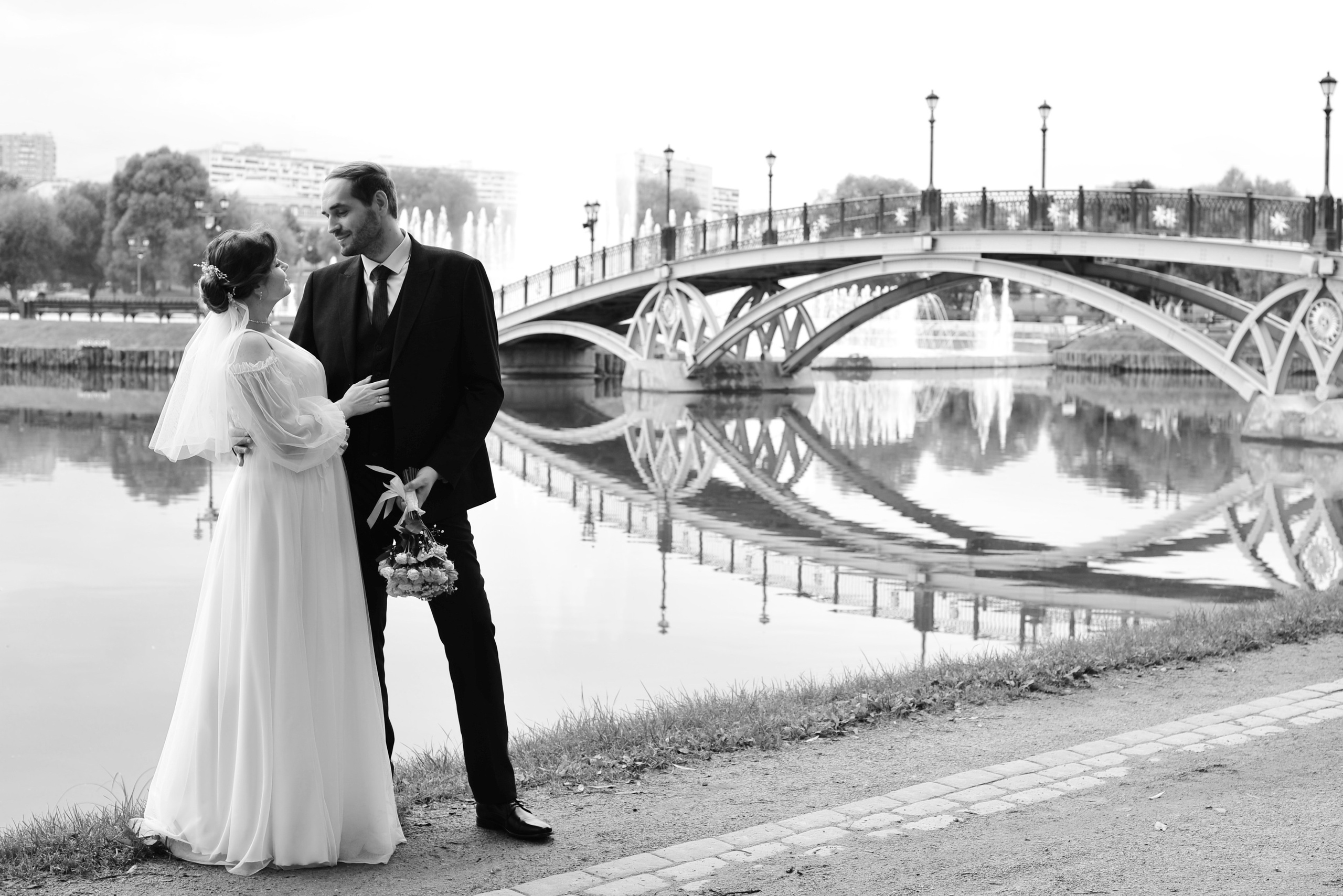 Свадьба в Царицыно пасмурным летним днем, жених и невеста смотрят друг на друга на фоне пруда и металлического моста,  черно-белая фотография
