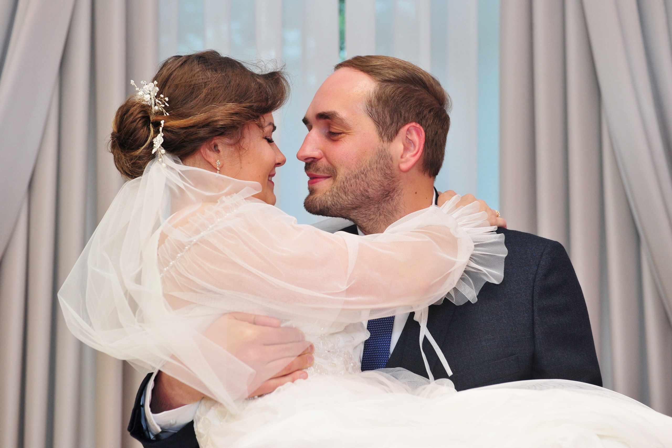 Свадьба в Царицыно пасмурным летним днем, невеста на руках у жениха в ЗАГСе перед выходом на улицу 