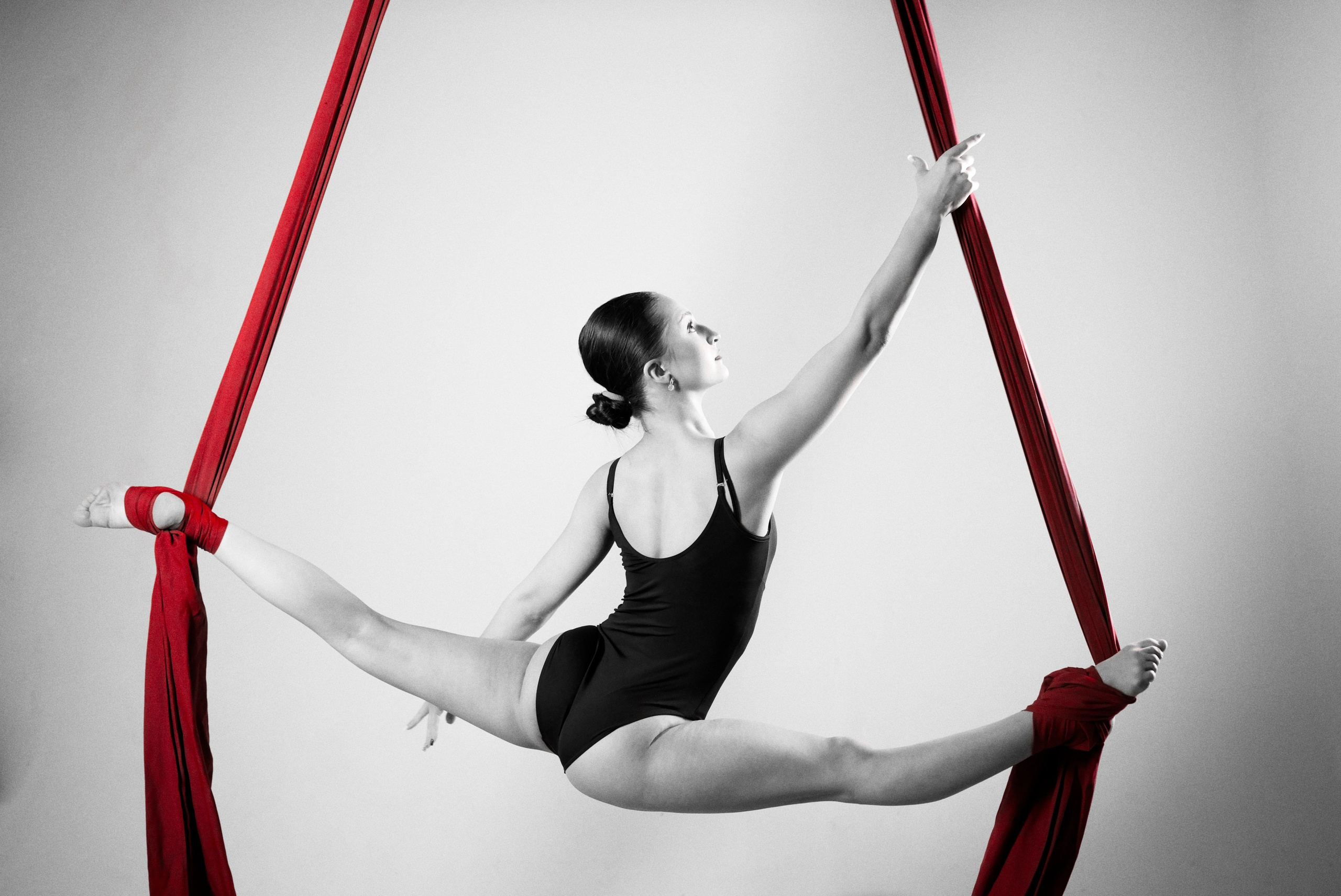 Безупречный горизонтальный шпагат в воздухе на красных полотнах, профессиональная спортивная съемка гимнастки