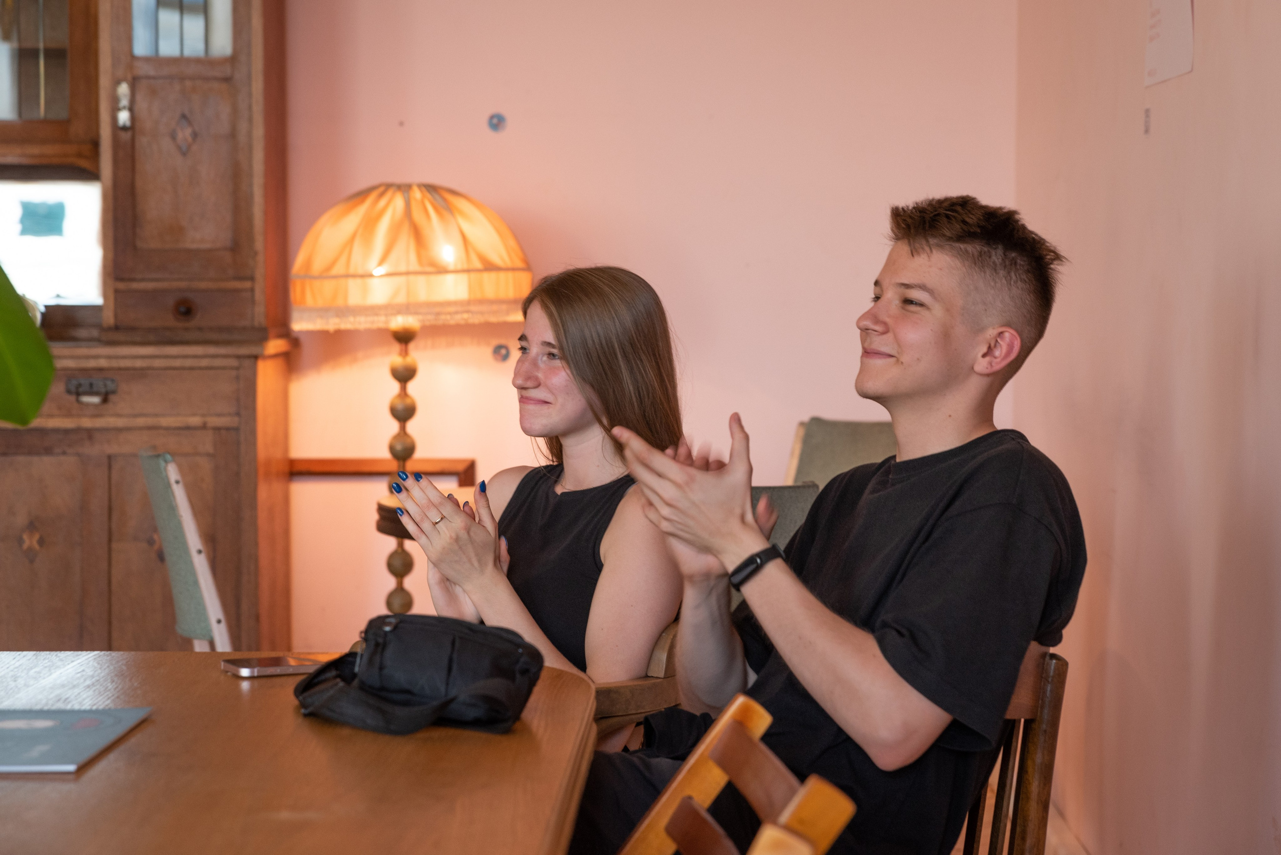 Молодой человек и девушка сидят за столом слушают музыку и аплодируют.