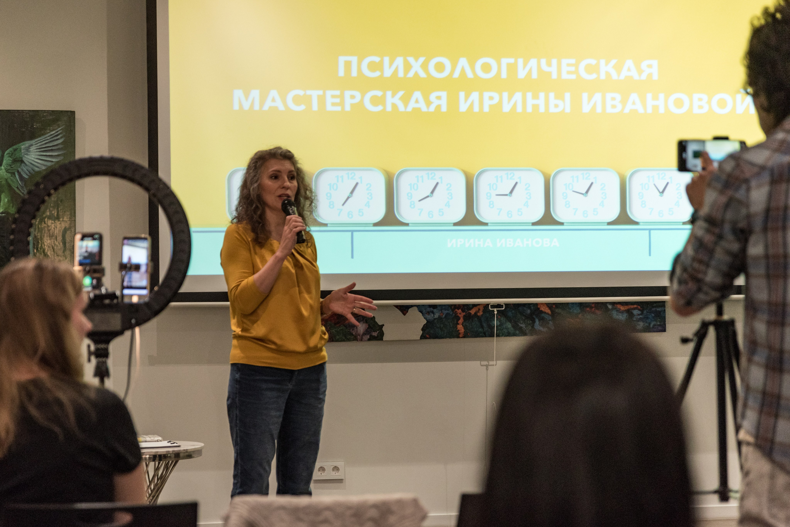 Ведущая семинара по психологии Ирина Иванова говорит в микрофон. На стене сзади презентация.