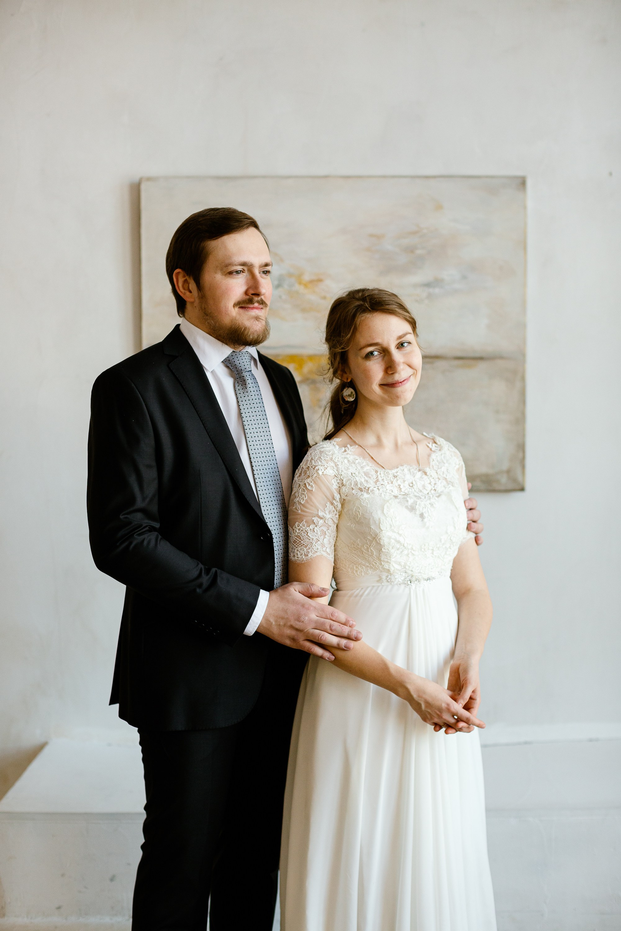 Жених и невеста в праздничной фотостудии. Жених в костюме, невеста в красивом белом платье. На фоне картина.