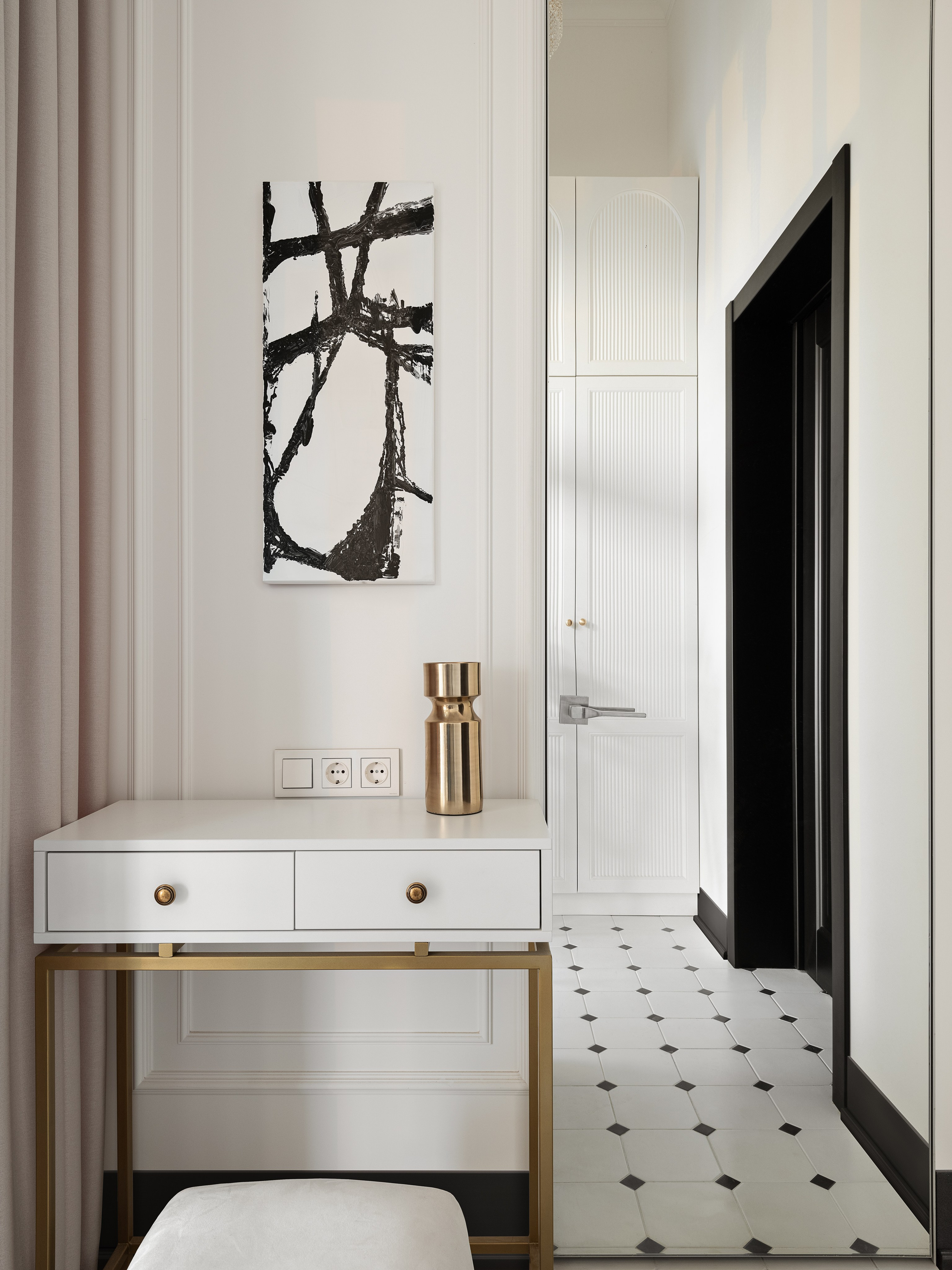 Интерьер прихожей с белой консолью и золотым декором, современная графика на стене, светлый пол с контрастным рисунком плитки, утончённые детали создают элегантную атмосферу, дизайнер Василисса Бачева, стилист Наталья Якушева, фото Сергей Денисенко.