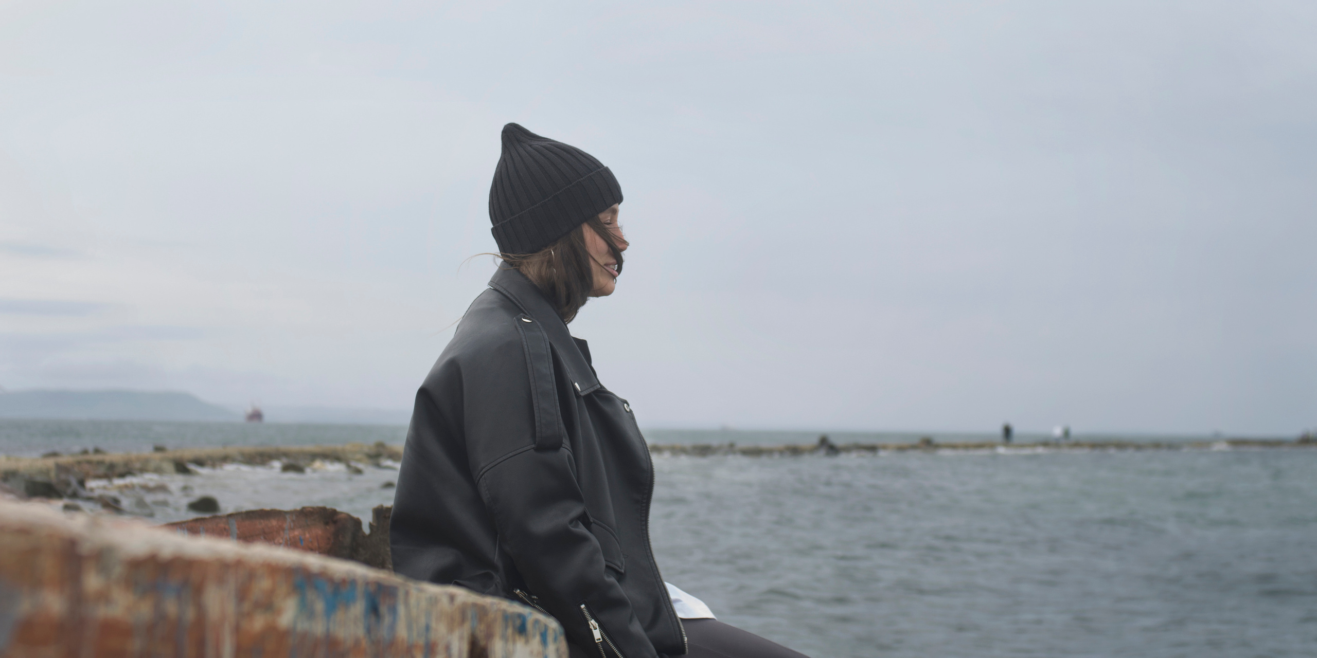 Девушка сидит на ржавой лодке, смотрит на море