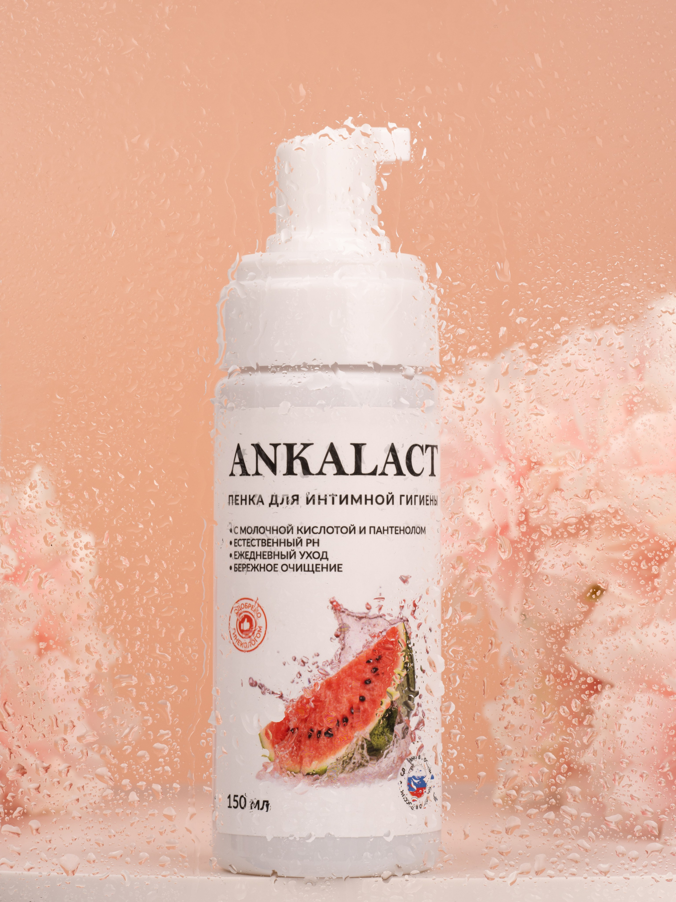 Белый флакон с дозатором ANKALACT с графикой арбуза на этикетке среди розовых губок и капель воды на светло-розовом фоне.