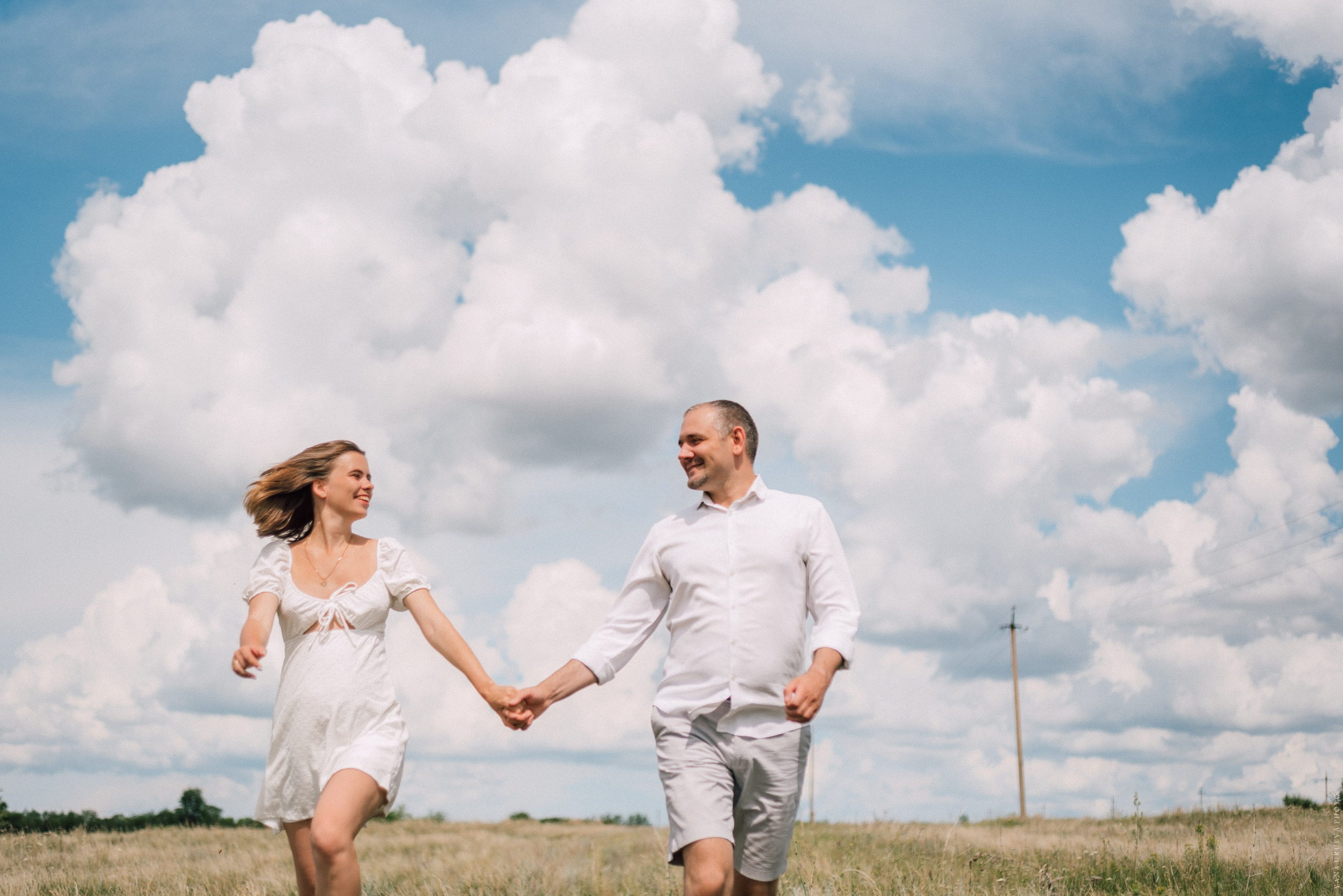 беременная съемка пара бежит по полю на фоне облаков