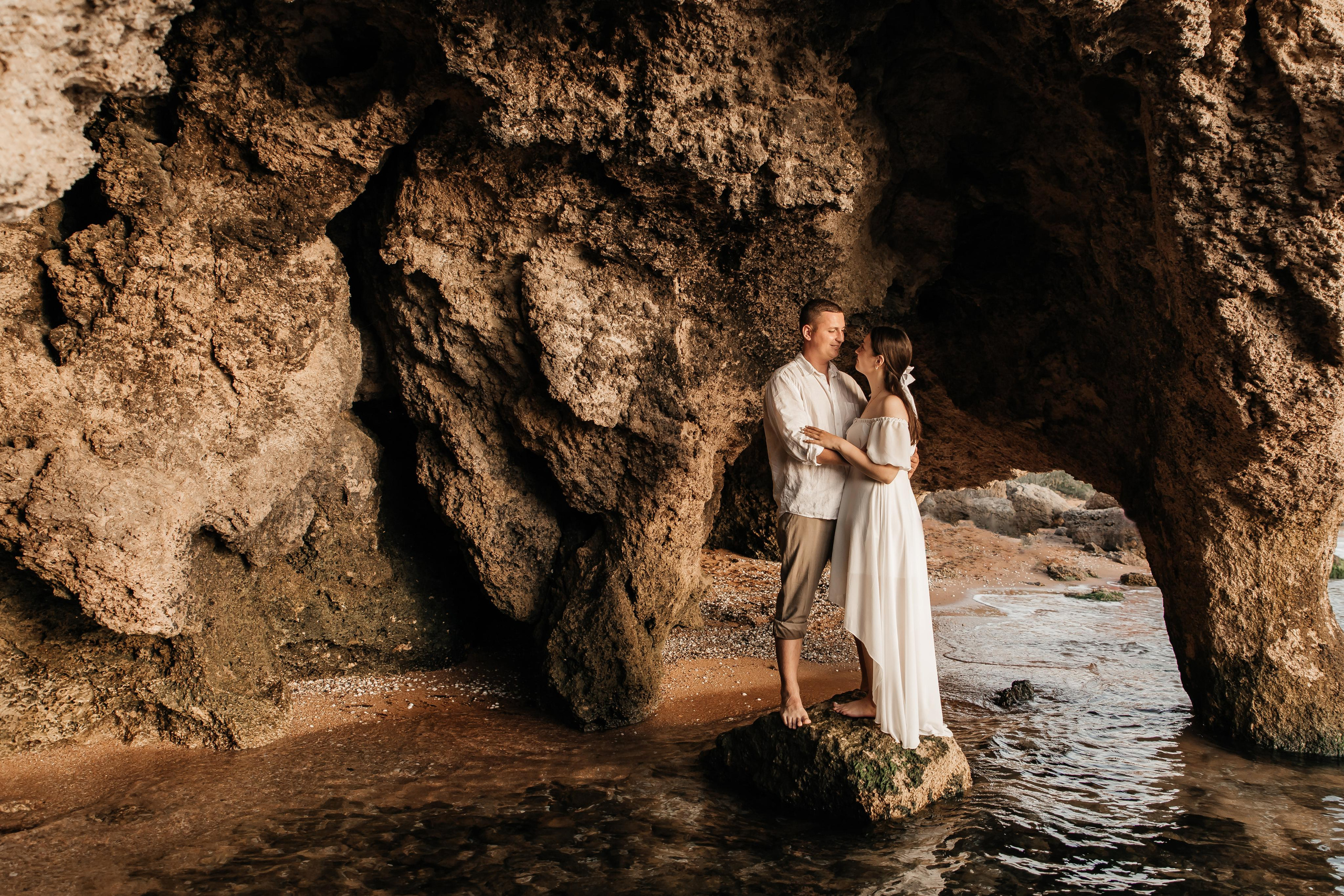 Девушка и парень в белых одеждах стоят на камне на морском берегу в гроте . 