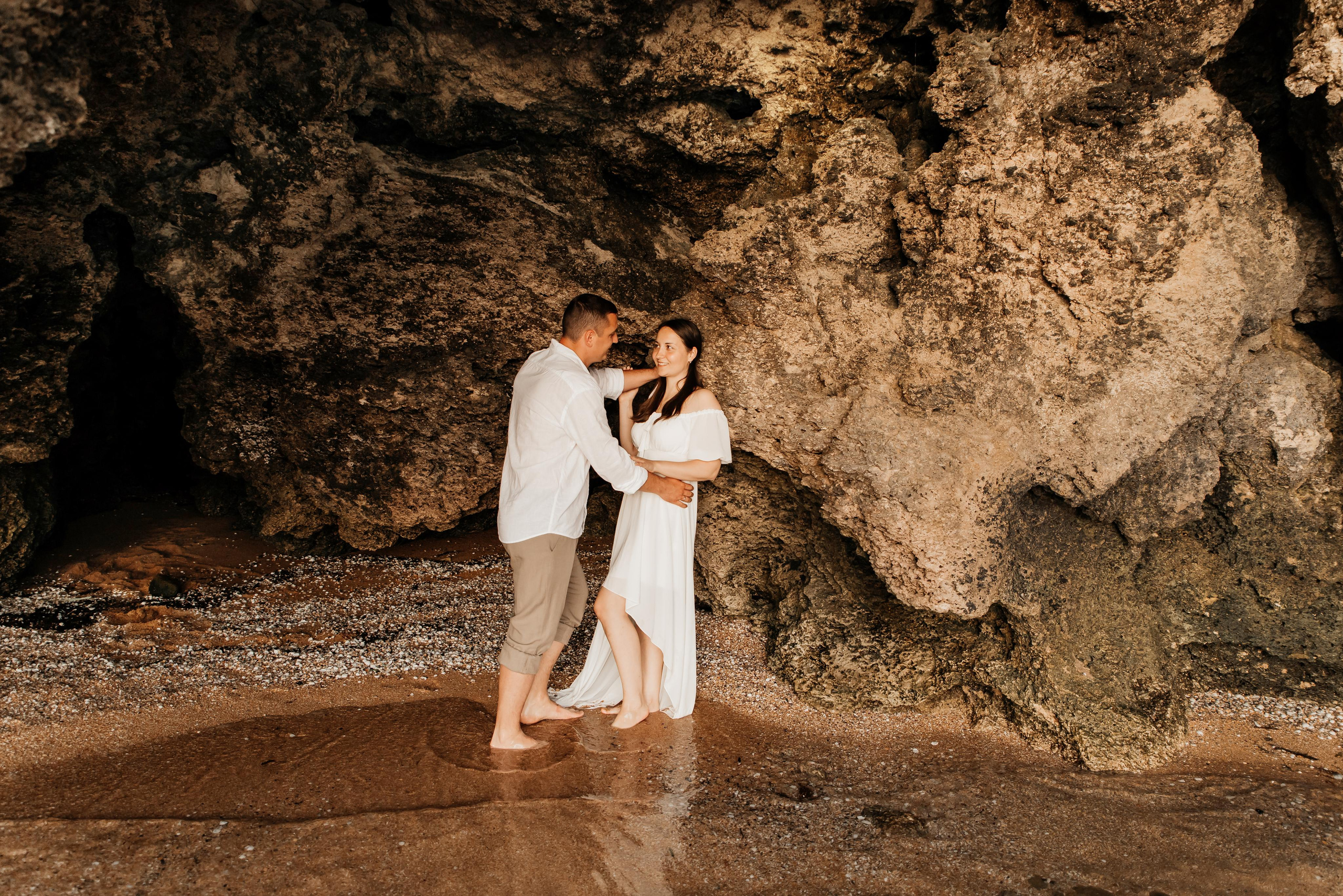 Девушка и парень смотрят друг на друга на берегу моря в скалистом гроте.